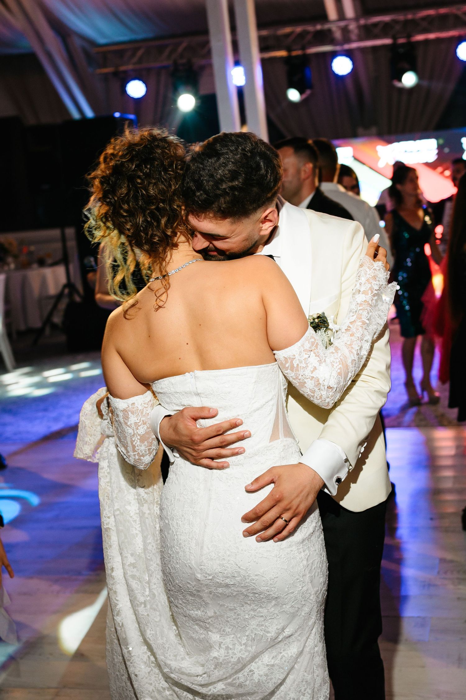 Bride and groom share their first dance, embracing closely in wedding attire at a reception venue.