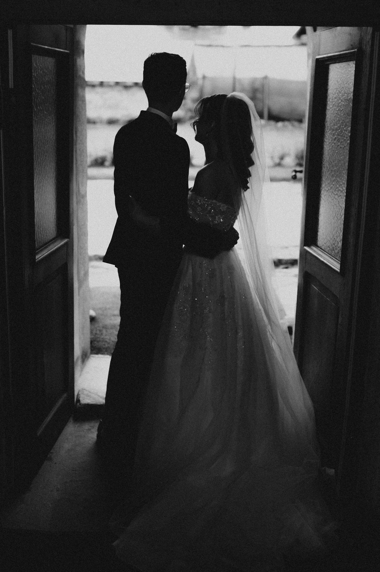 Black and white silhouette of bride and groom embracing in doorway on wedding day.
