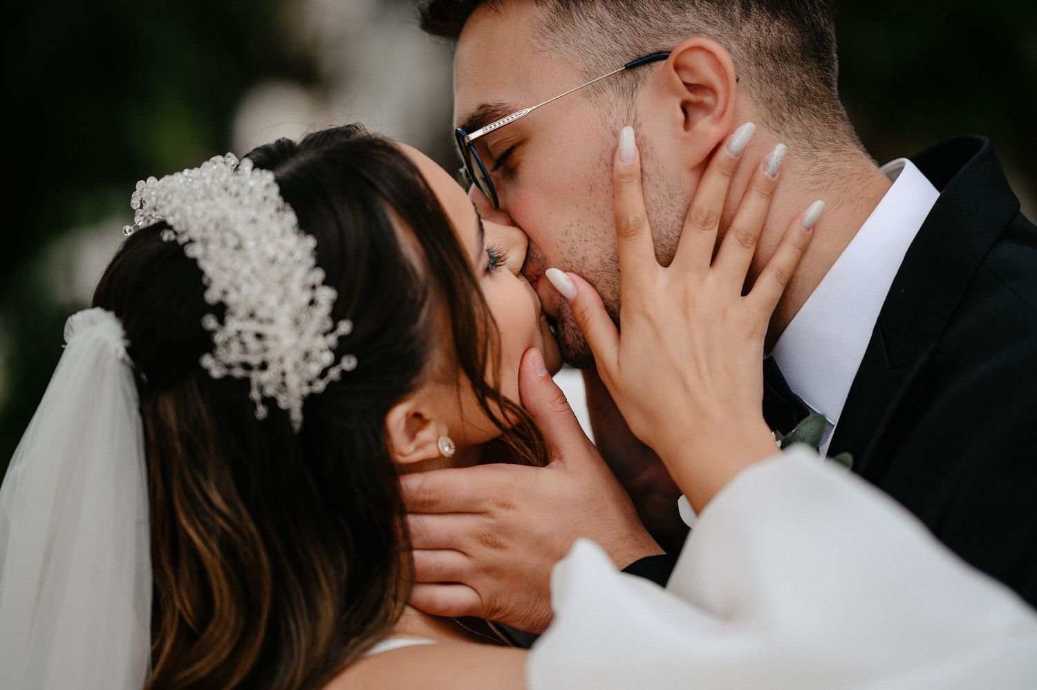 Bride and groom share romantic kiss closeup with bride wearing pearl hair accessory and veil.