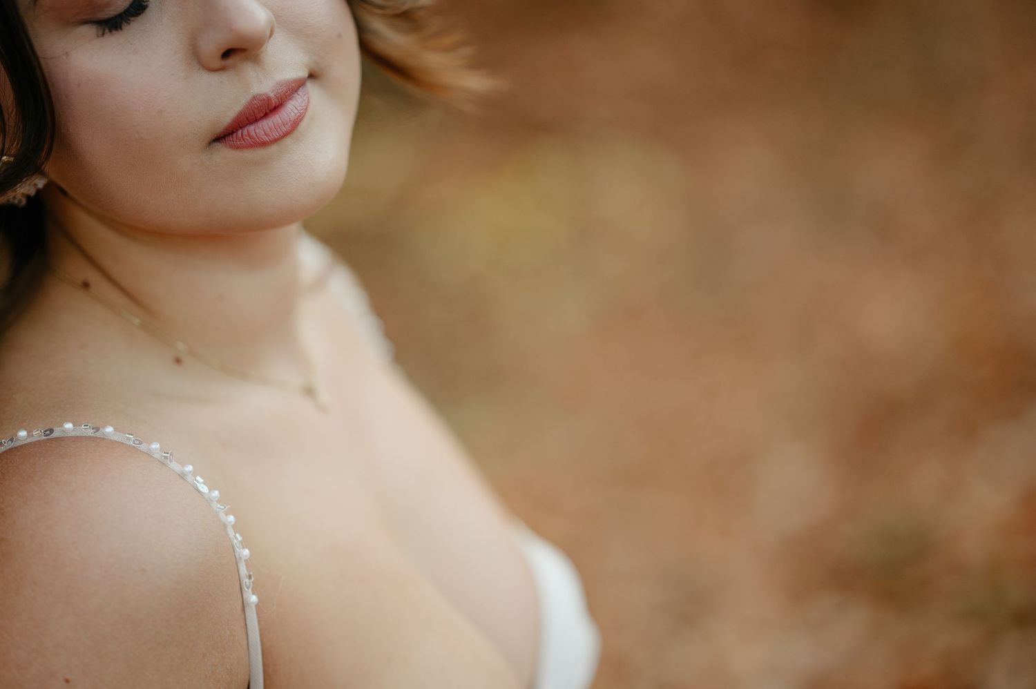 A bride in a beaded white gown poses outdoors with a soft autumn bokeh background.