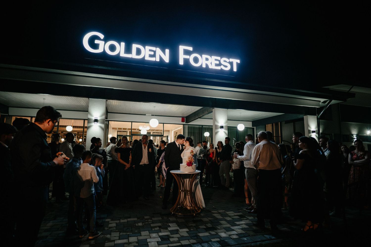 Wedding guests gathered outside Golden Forest venue at night.