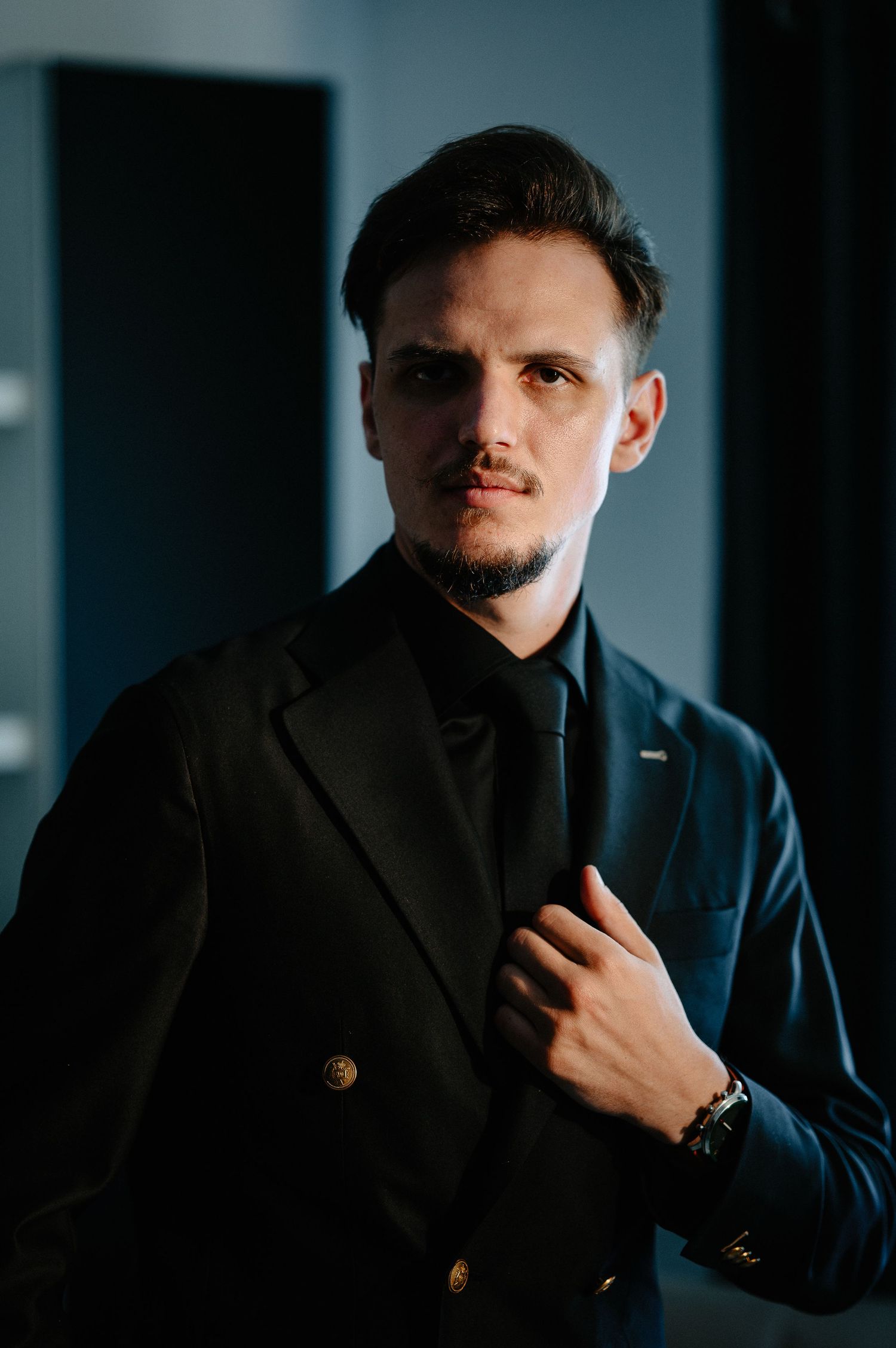 Groom in a dark double-breasted suit with gold buttons posing in dramatic lighting.