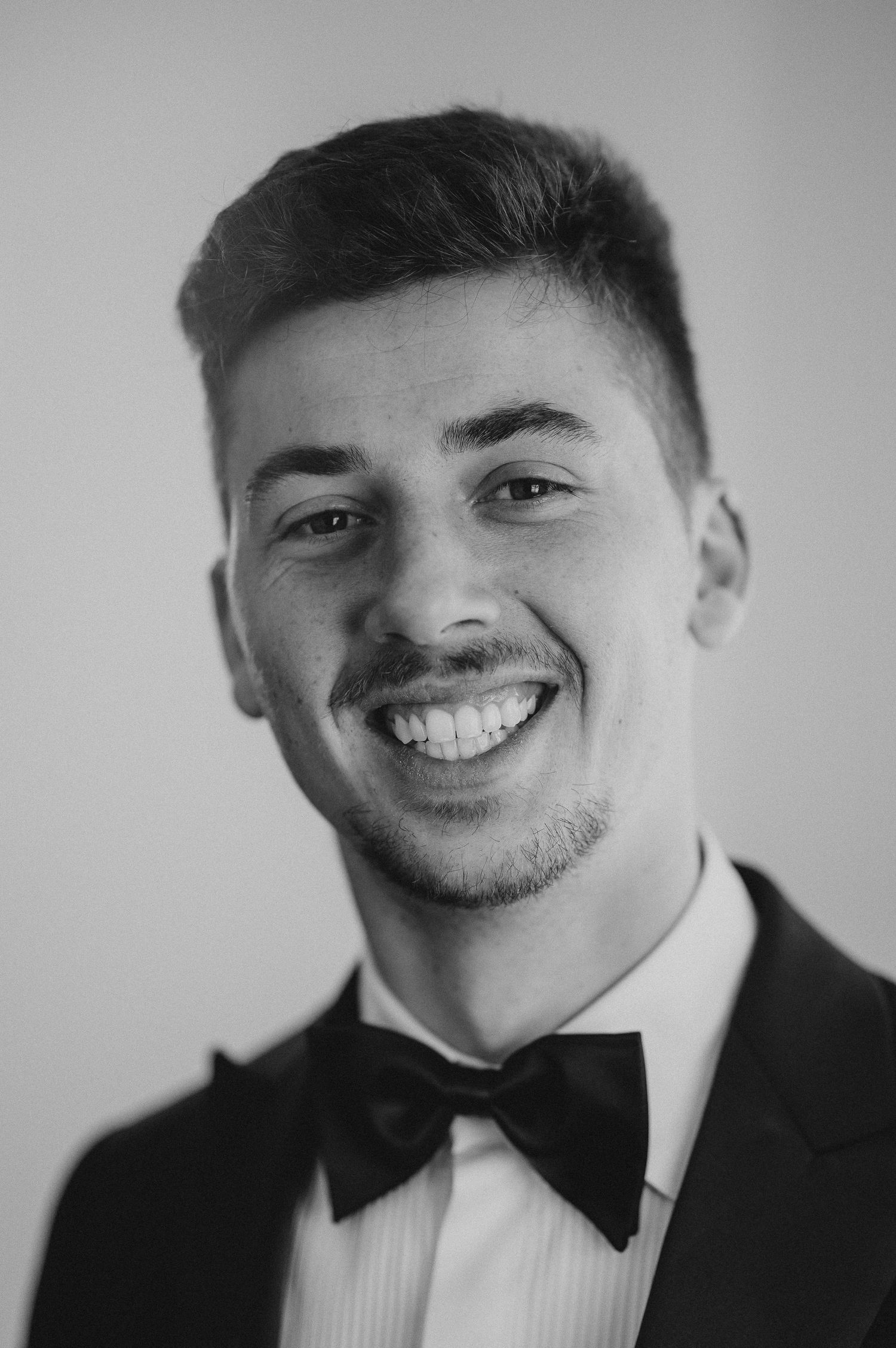 Black and white portrait of happy groom in tuxedo with bow tie.