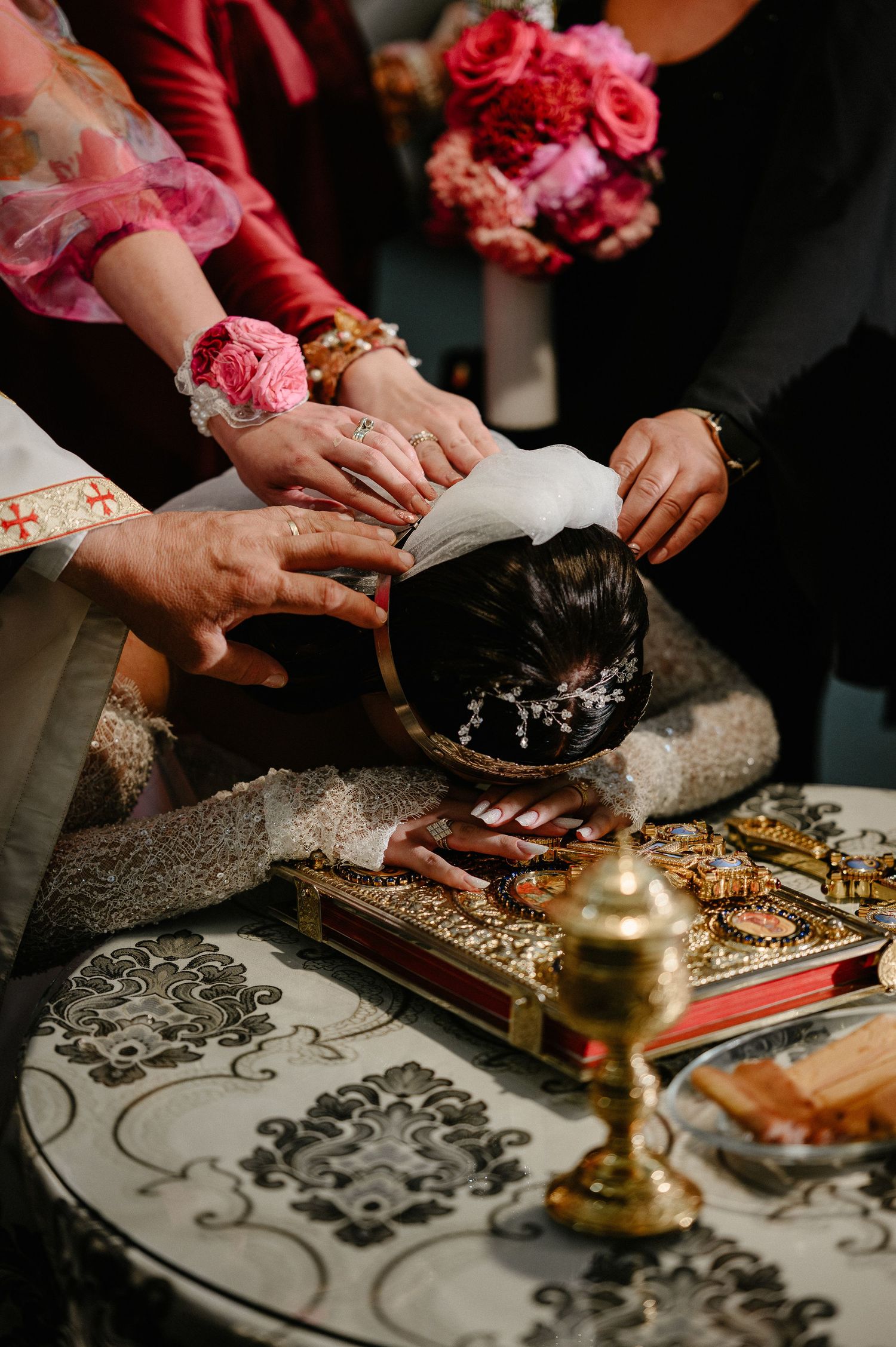 Hands placing a wedding crown on bride's head during Orthodox marriage ceremony with golden artifacts.