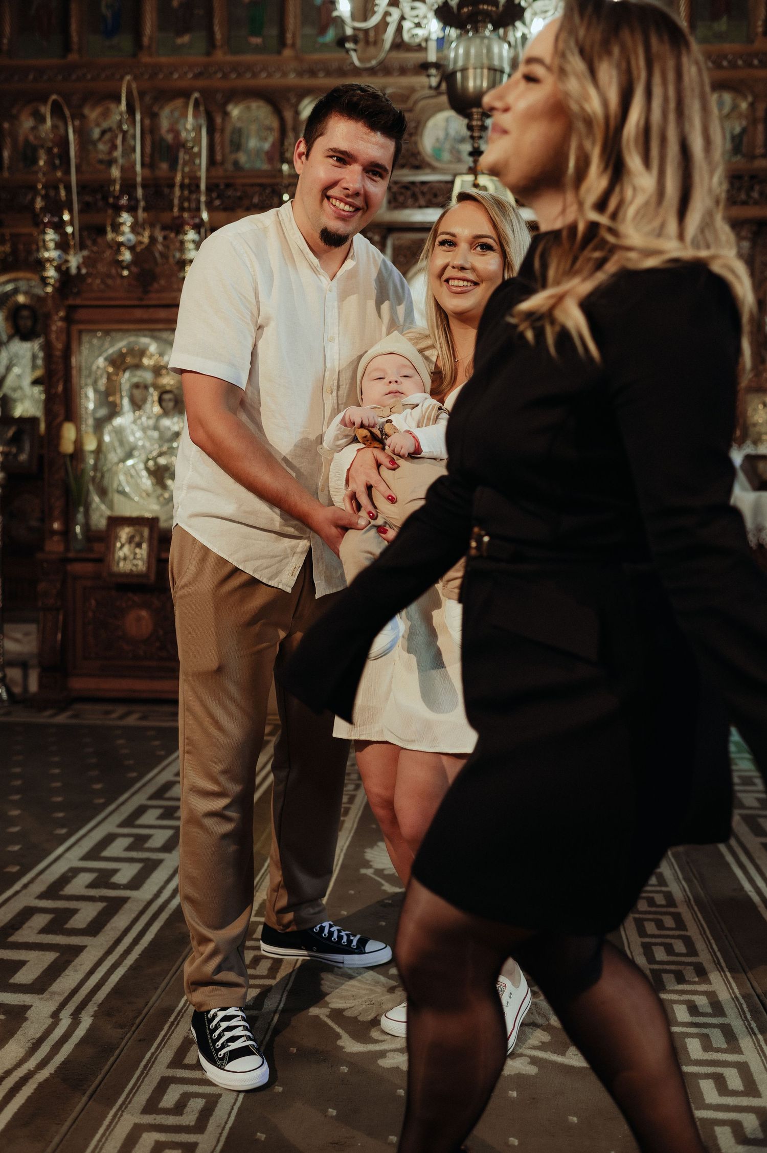 Happy family with newborn baby socializes with guest in decorated Orthodox church.