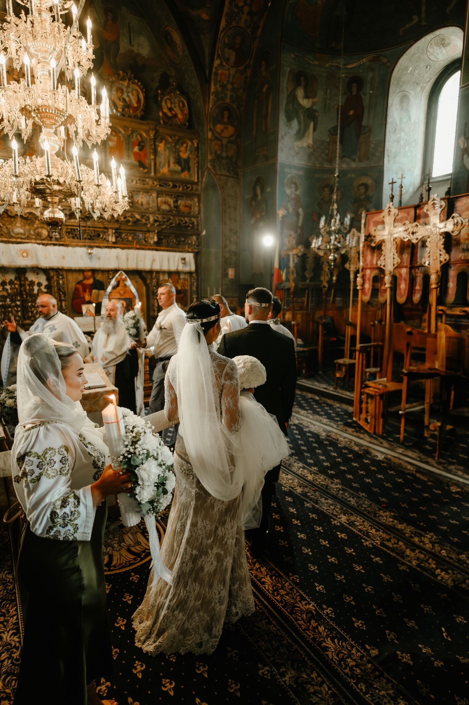 Bride and groom stand at altar in ornate Orthodox church surrounded by candles and icons.
