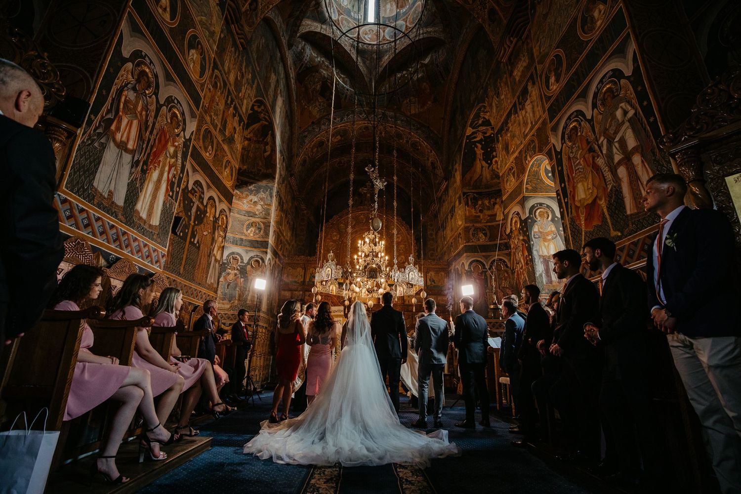 Bride and groom exchange vows inside an ornate Orthodox church with stunning frescoes and golden chandelier.