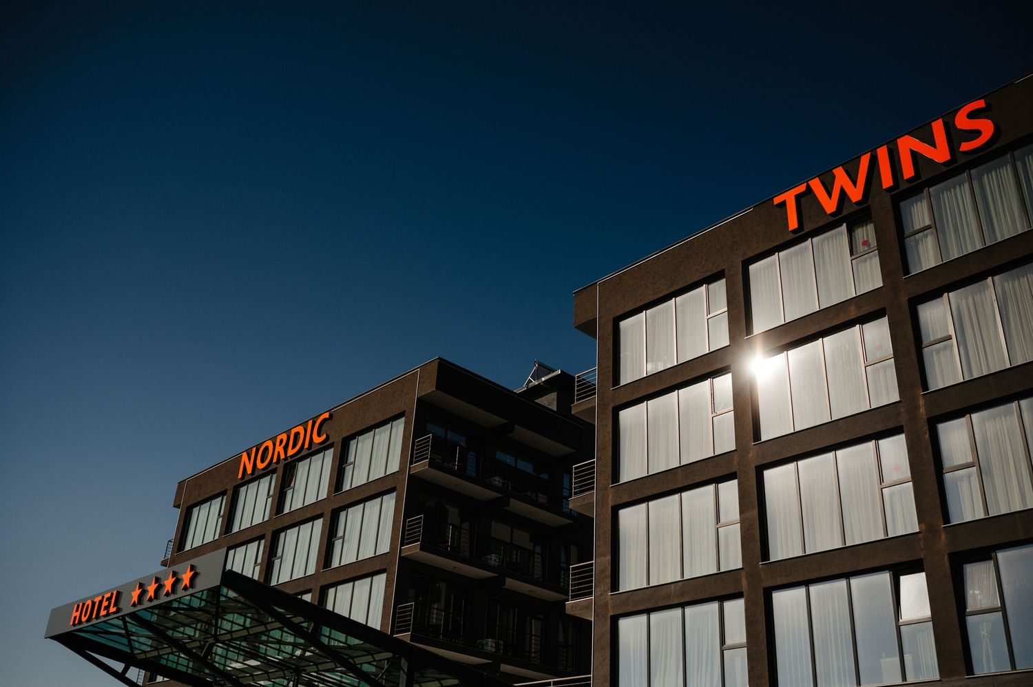 Nordic Hotel Twins illuminated sign on modern building facade against deep blue evening sky.