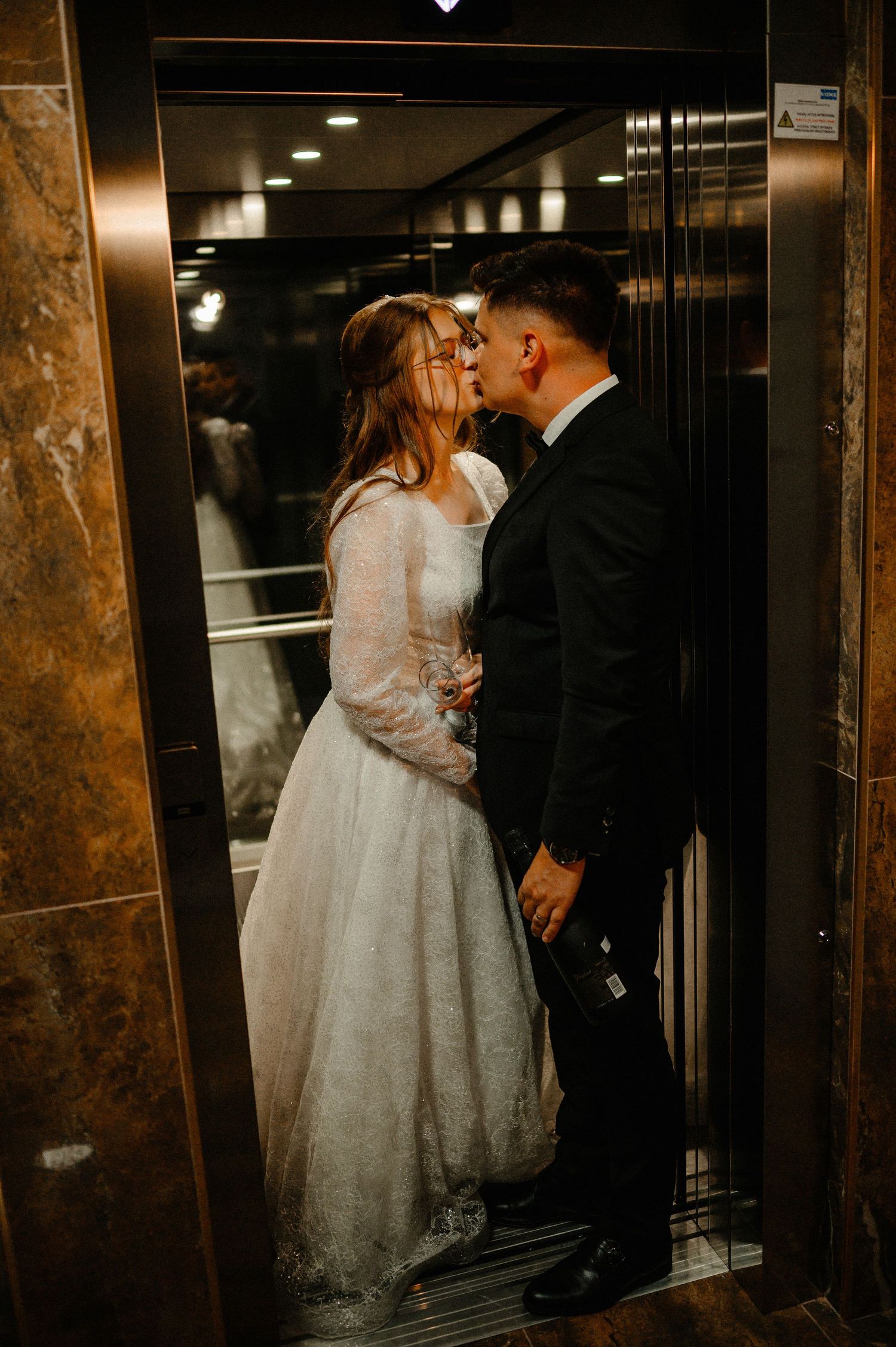 Bride and groom sharing a kiss inside a hotel elevator on their wedding day.