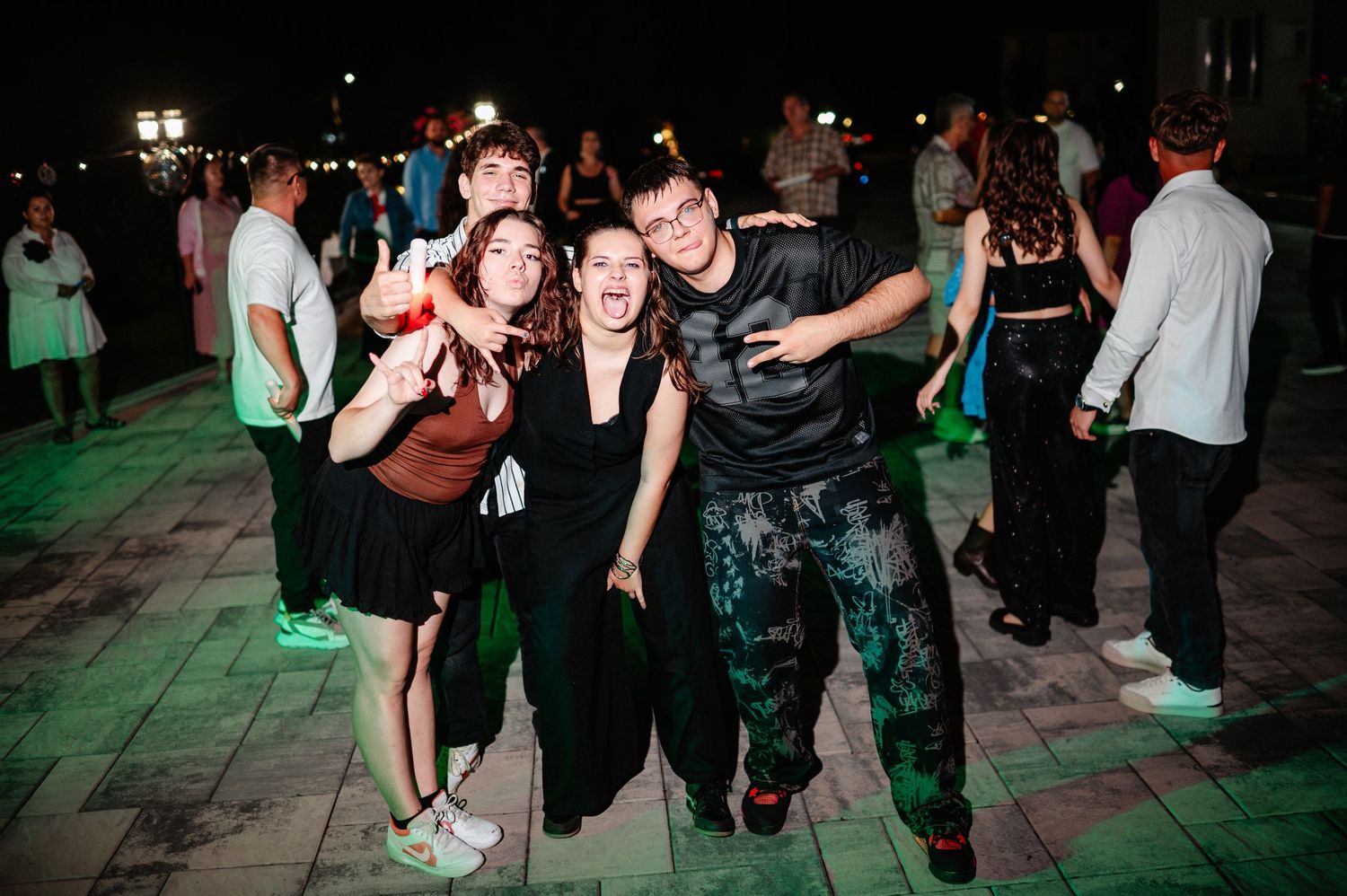 Four friends posing together and smiling at outdoor night party under green lights on dance floor.