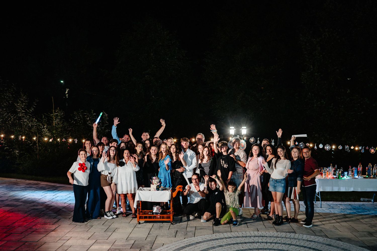 Large group of smiling guests posing together at a festive outdoor nighttime birthday party.