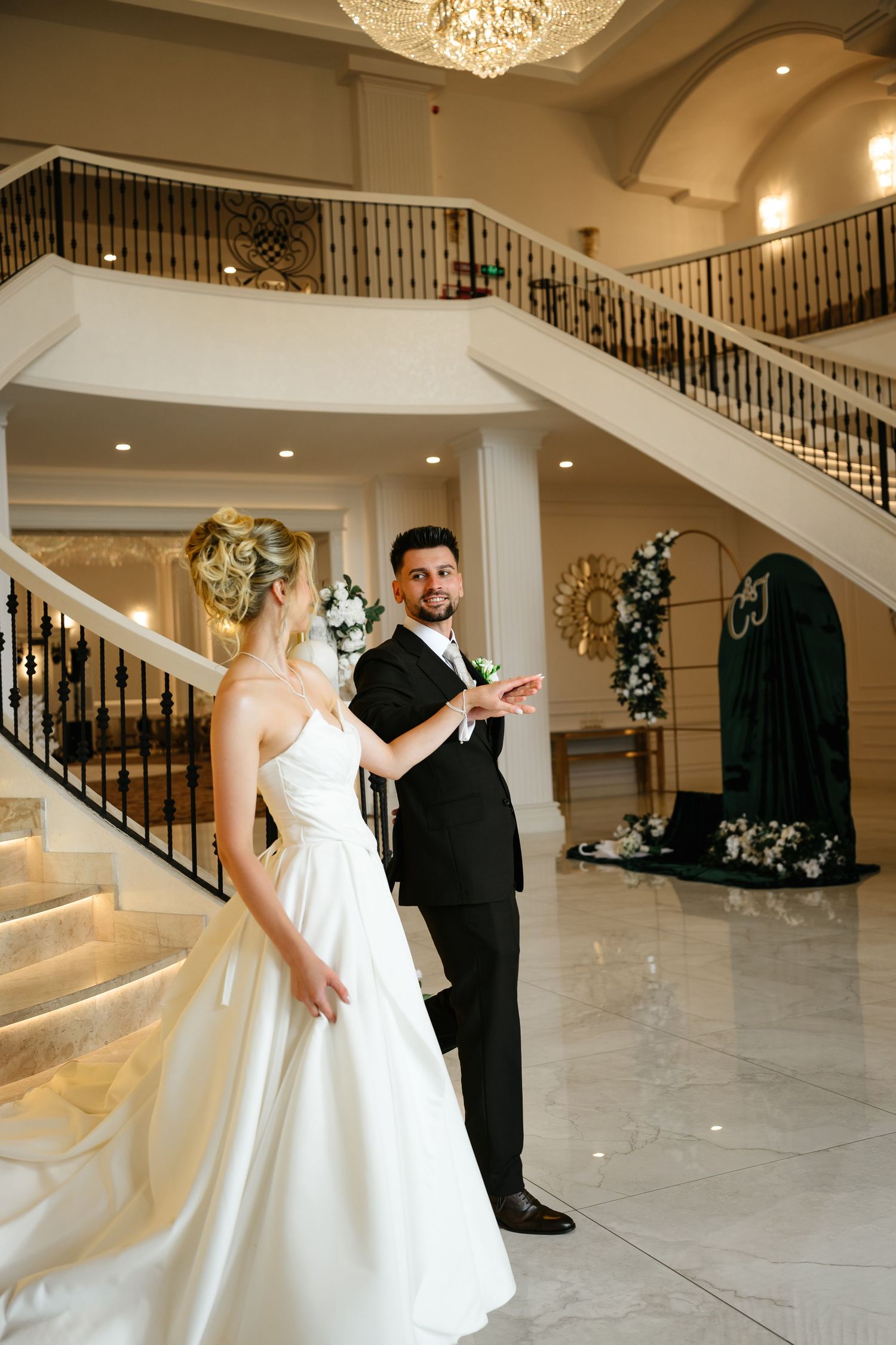 Bride and groom share a romantic first dance moment on marble floors of an elegant wedding venue with grand staircase.