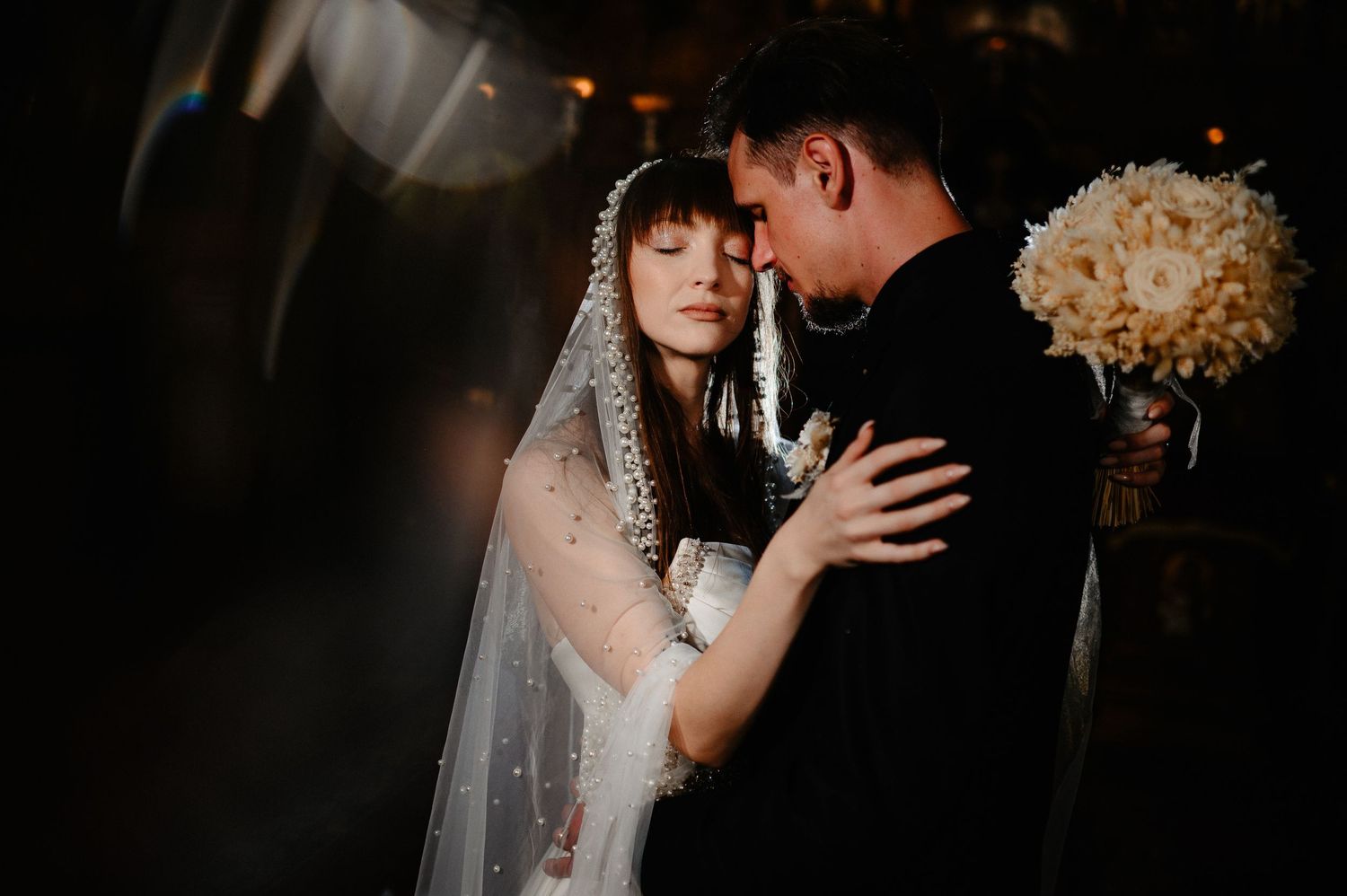 Bride and groom share intimate first dance moment in dim romantic lighting at wedding reception.