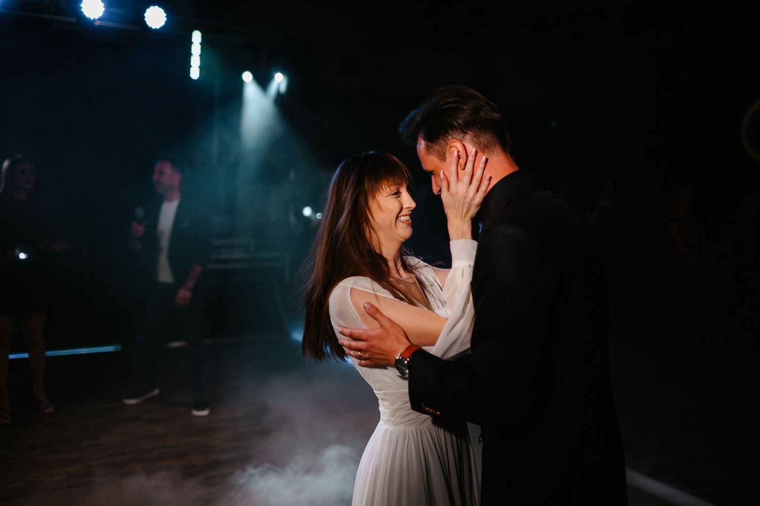 Couple sharing intimate first dance moment on foggy stage with dramatic lighting at wedding reception.