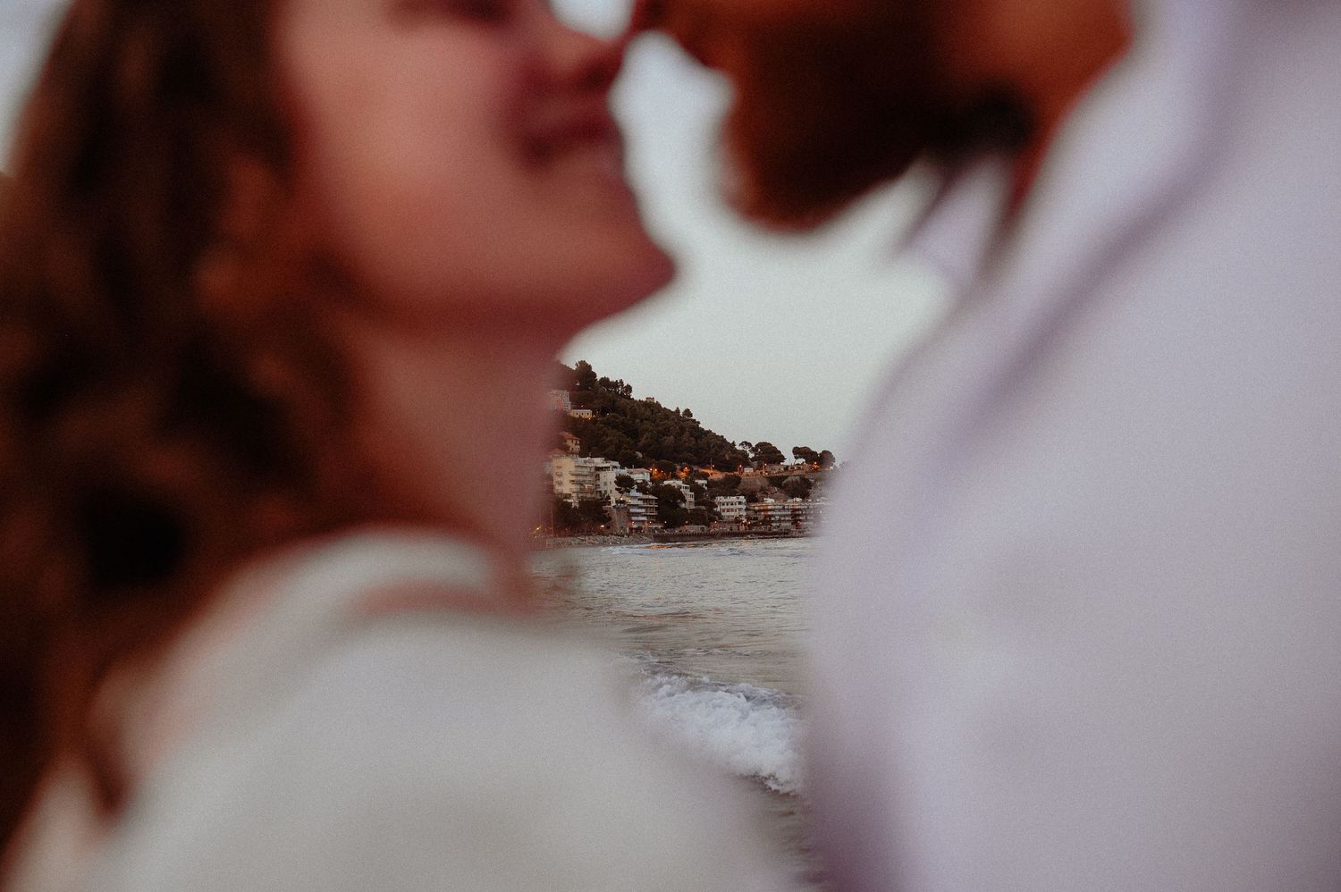 Romantic close-up of couple nearly kissing with a coastal village blurred in the background.