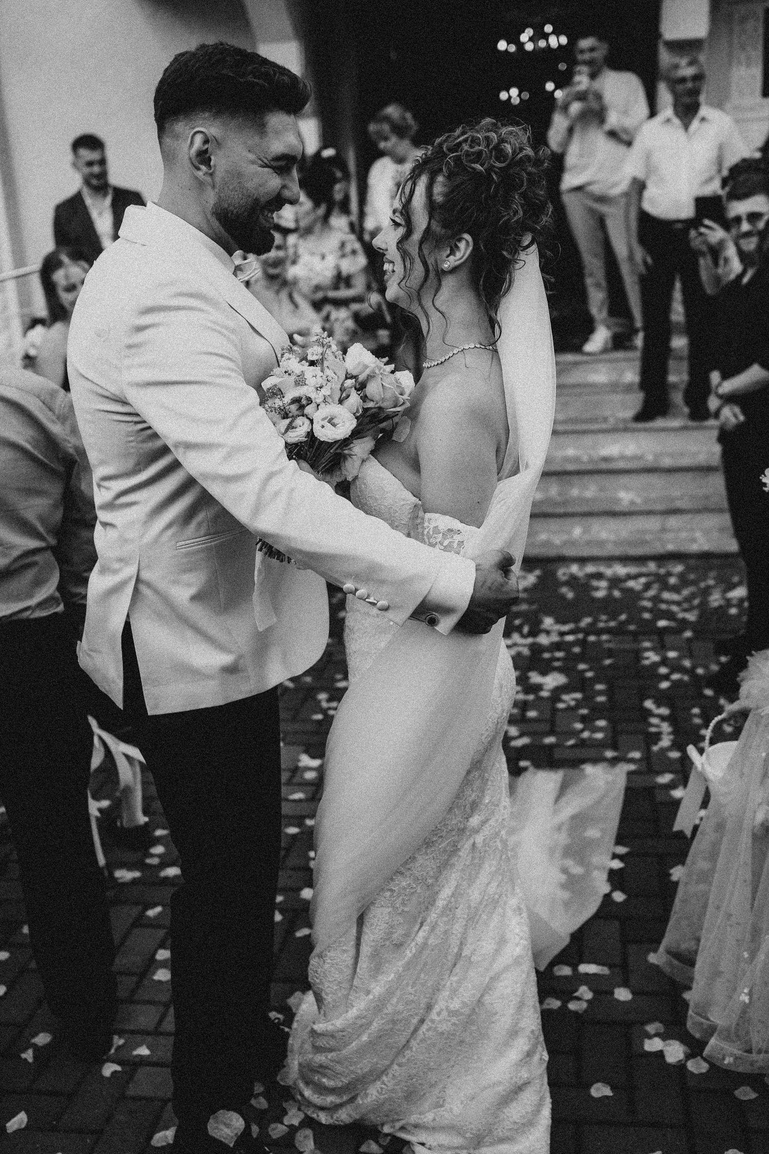 Black and white photo of a joyful bride and groom embracing after their wedding ceremony with confetti falling.