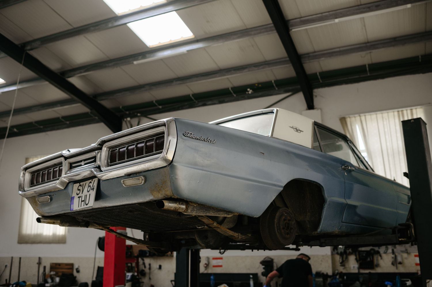 Vintage blue classic car elevated on a hydraulic lift inside an auto repair garage workshop.