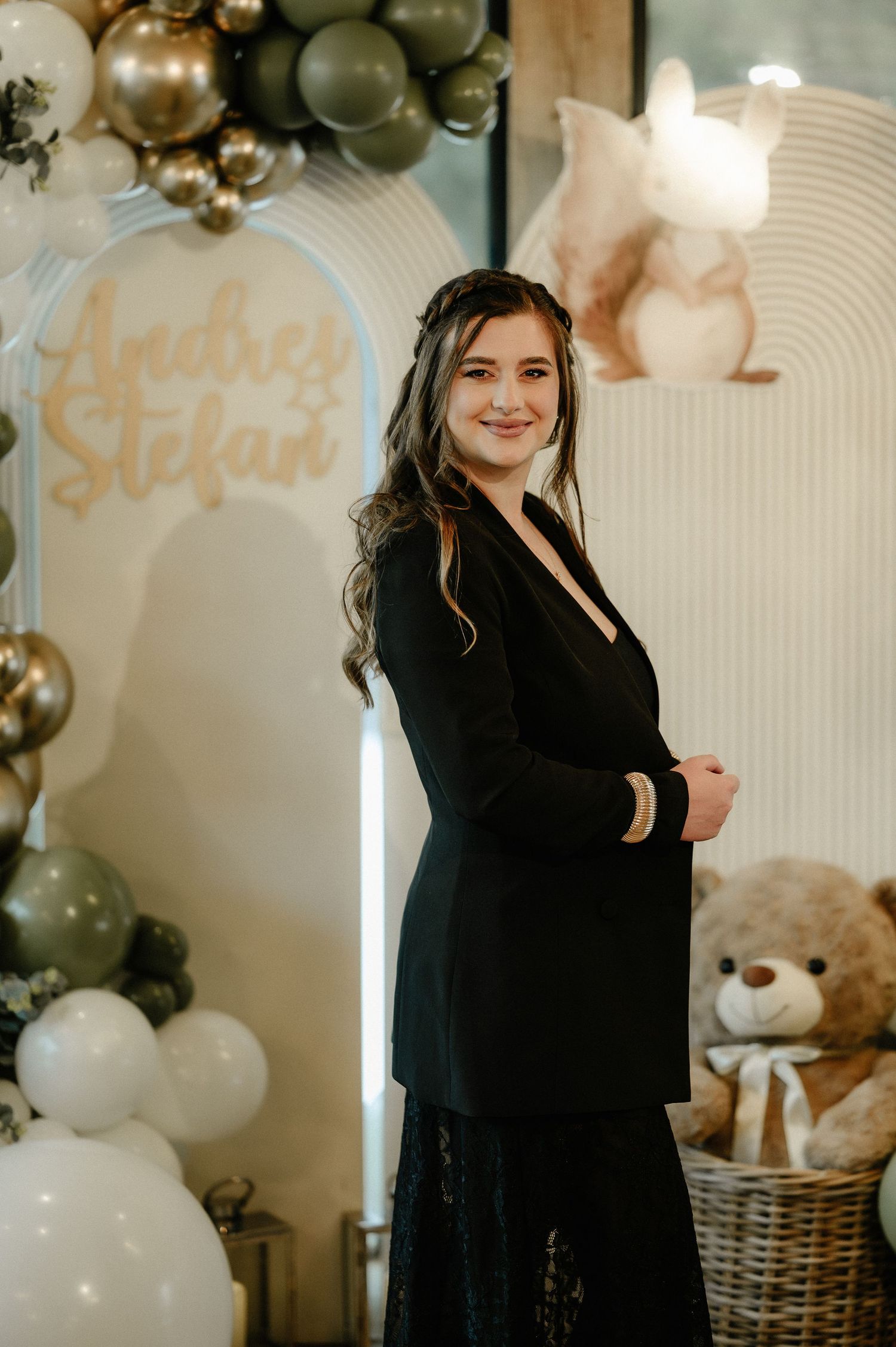 Young woman in black blazer smiling at a baby shower with balloon arch and teddy bear decor.
