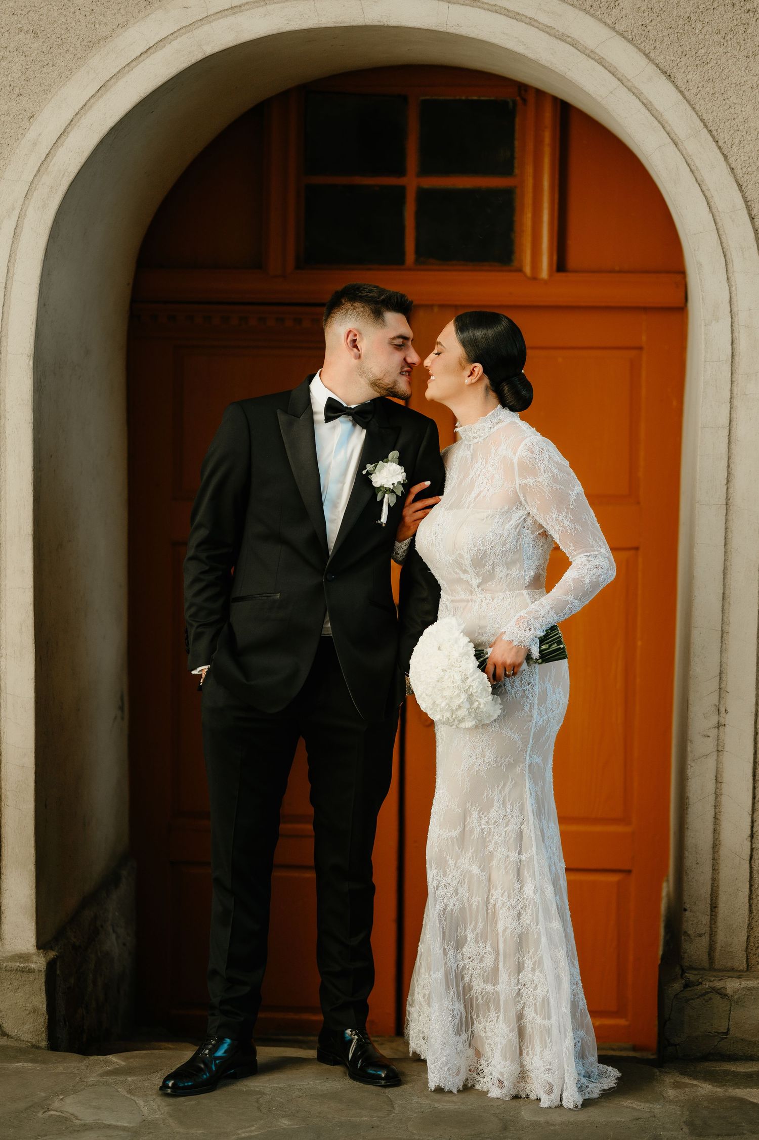 Bride and groom sharing a romantic moment in front of an orange arched church doorway.