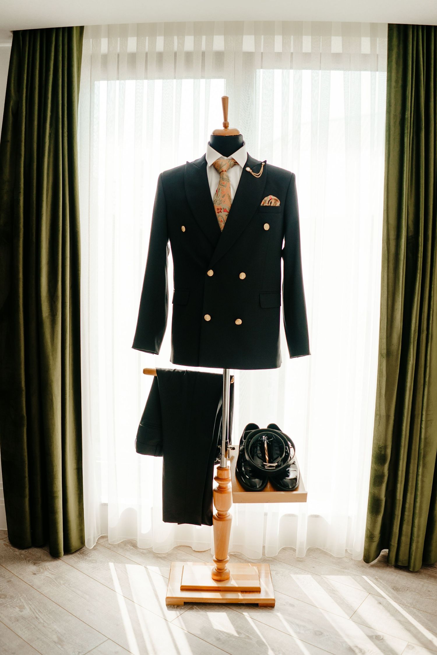 Black double-breasted suit displayed on mannequin stand by window with gold buttons and paisley tie.