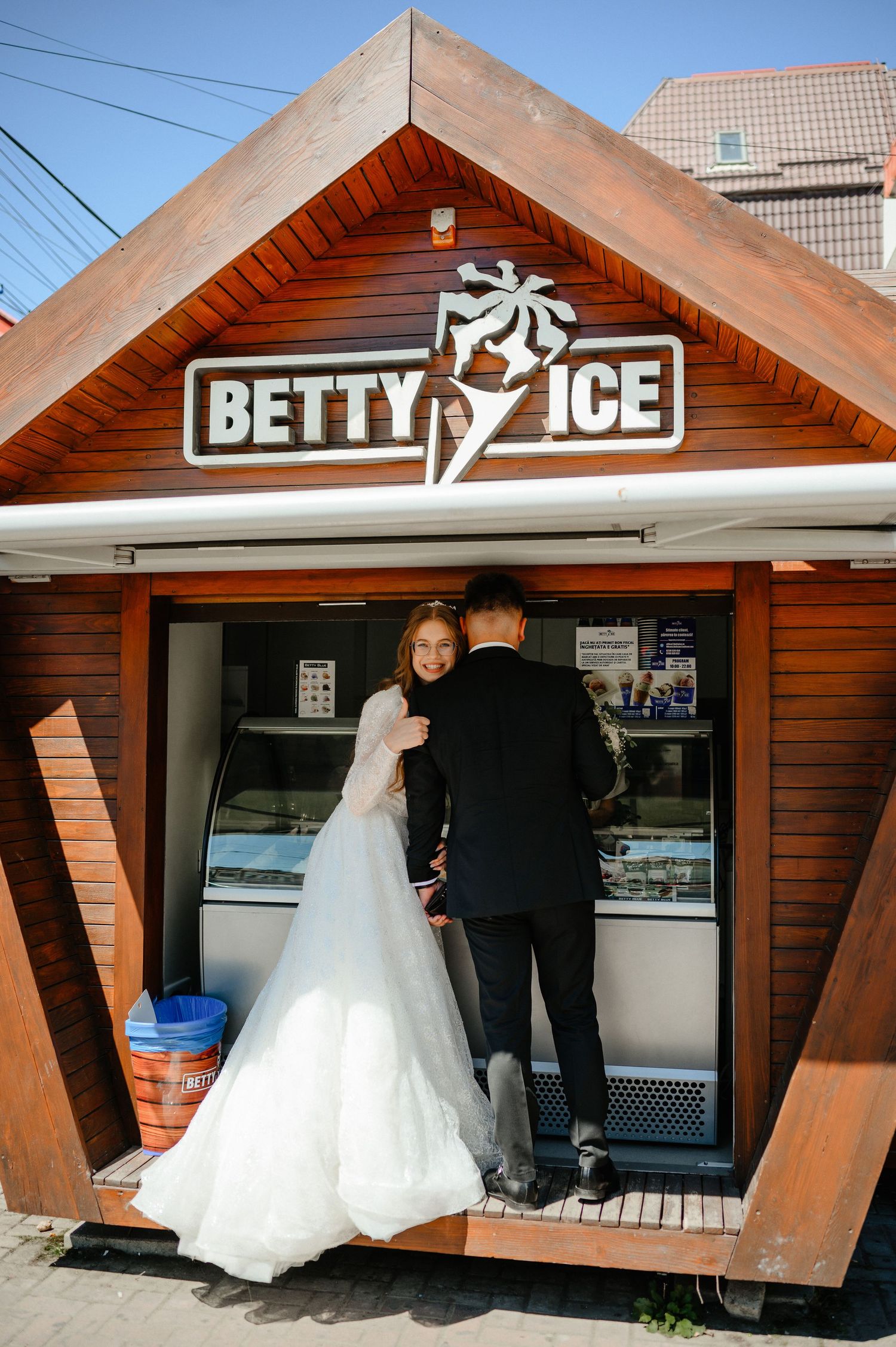 Bride and groom in wedding attire stopping at Betty Ice cream shop together.