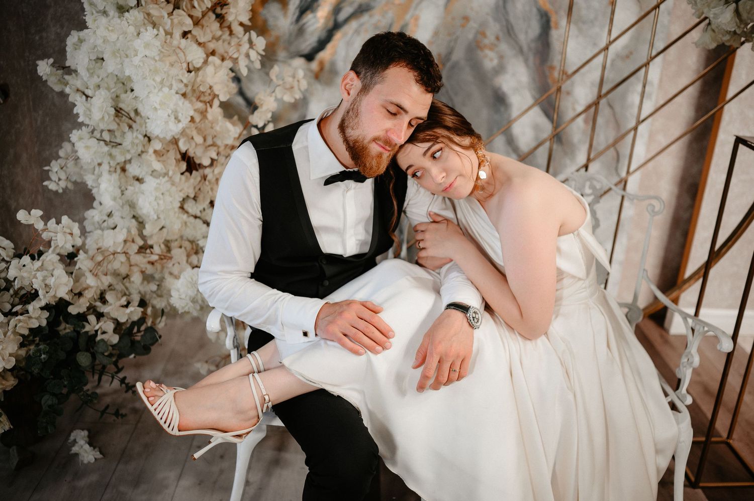 Bride resting her head on groom's shoulder while seated near white cherry blossom decor.