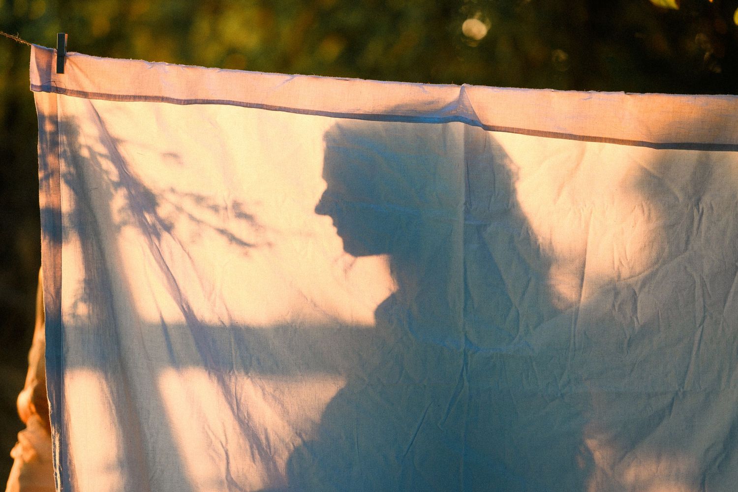 Silhouette of a woman projected on a white cloth sheet hanging outdoors in warm golden sunlight.