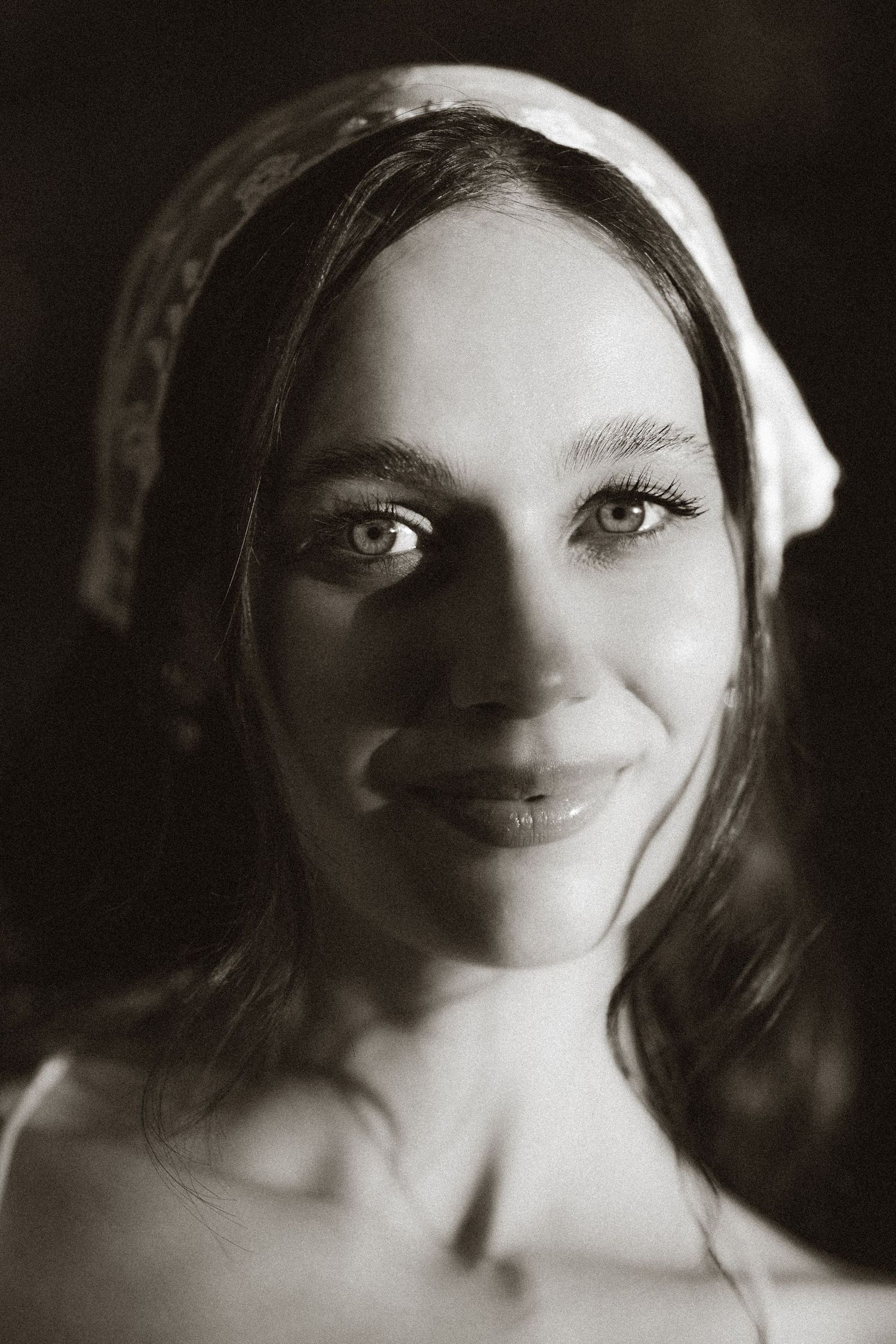 Black and white portrait of a young woman wearing a headscarf, smiling softly at the camera.