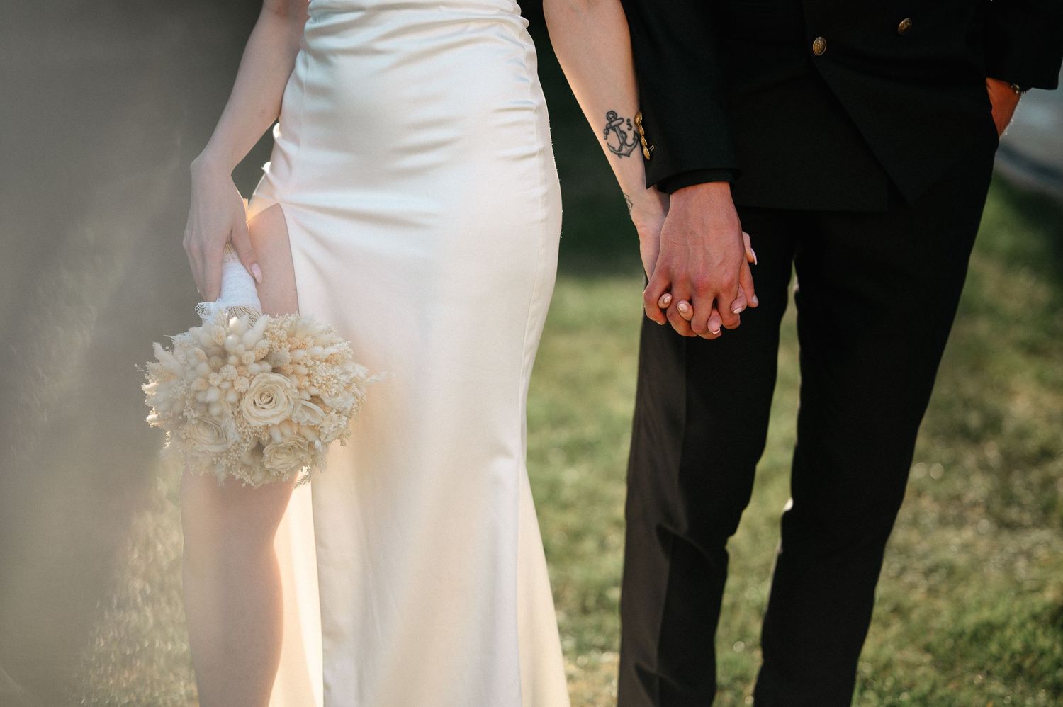 Close-up of bride and groom holding hands, bride in white gown holding white rose bouquet.