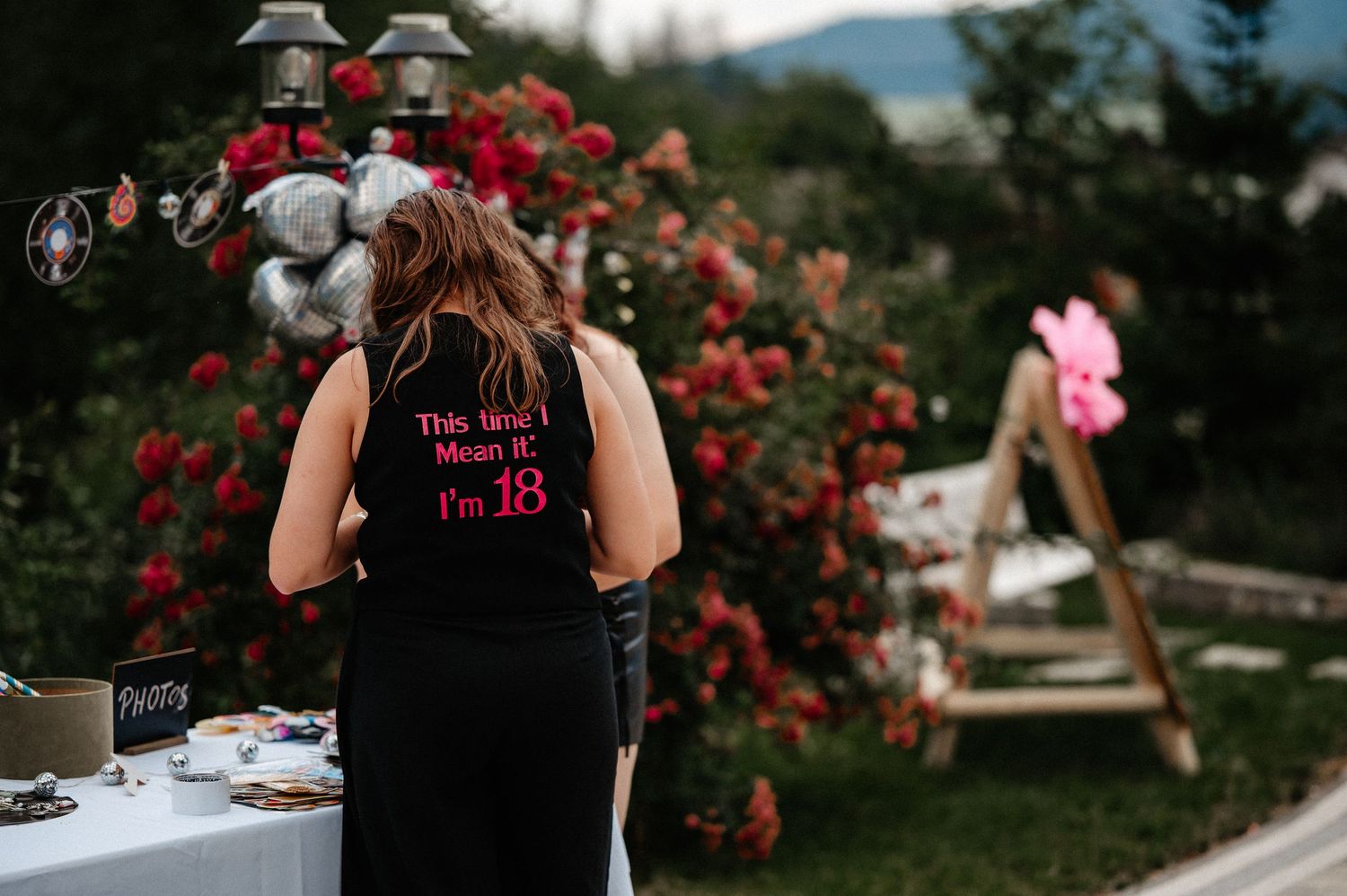 Person wearing a black apron reading This Isnt Mean It Im 18 standing at an outdoor party table.
