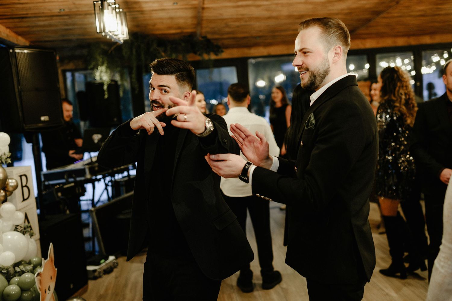 Two men in black suits laughing and celebrating at an elegant indoor party event.