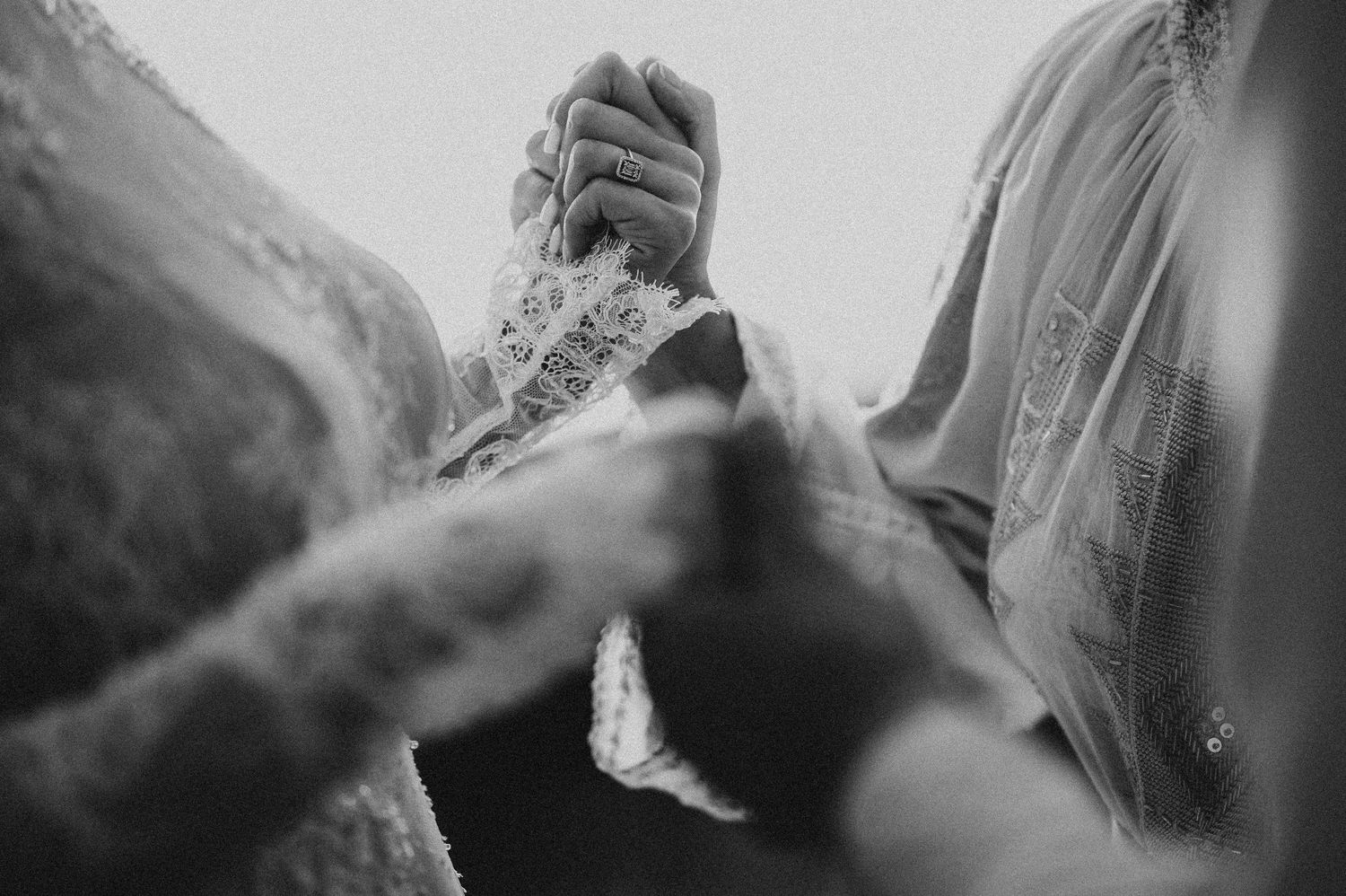 Close-up black and white photo of bride and groom holding hands during wedding ceremony.