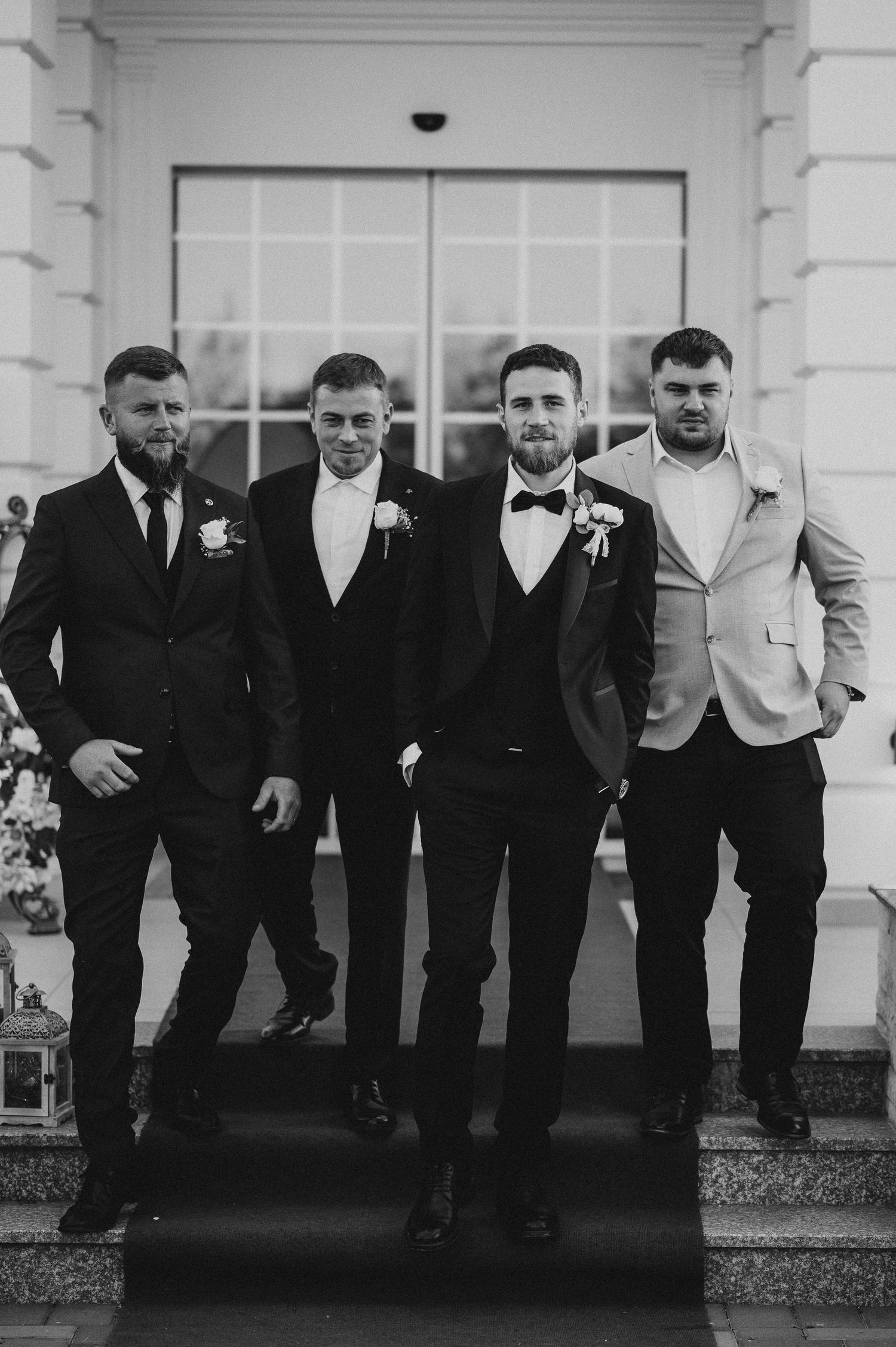 Groom with three groomsmen in suits posing on steps in black and white photo.