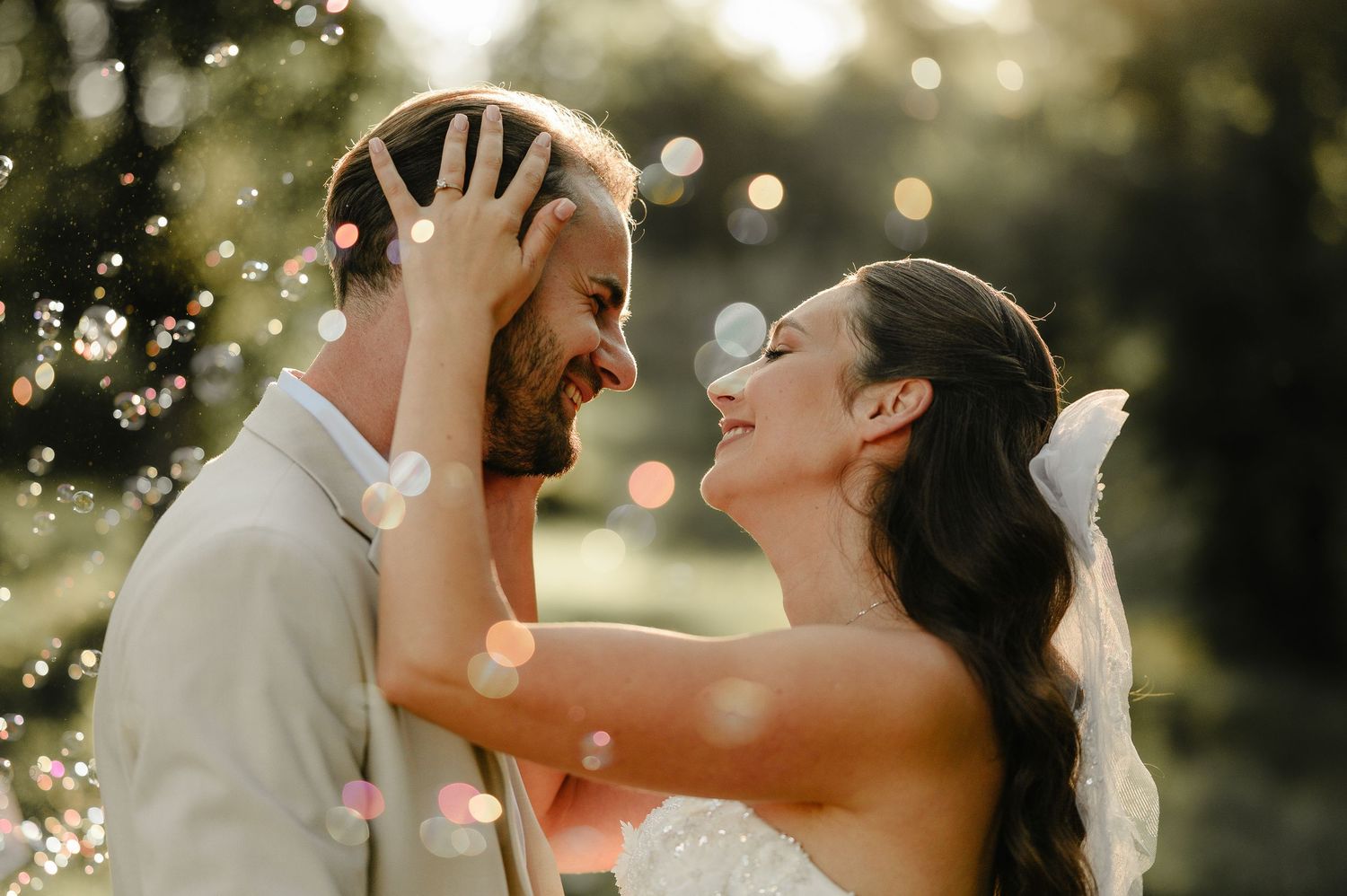 Joyful bride and groom laughing together with bokeh light effects in sunny outdoor wedding portrait.