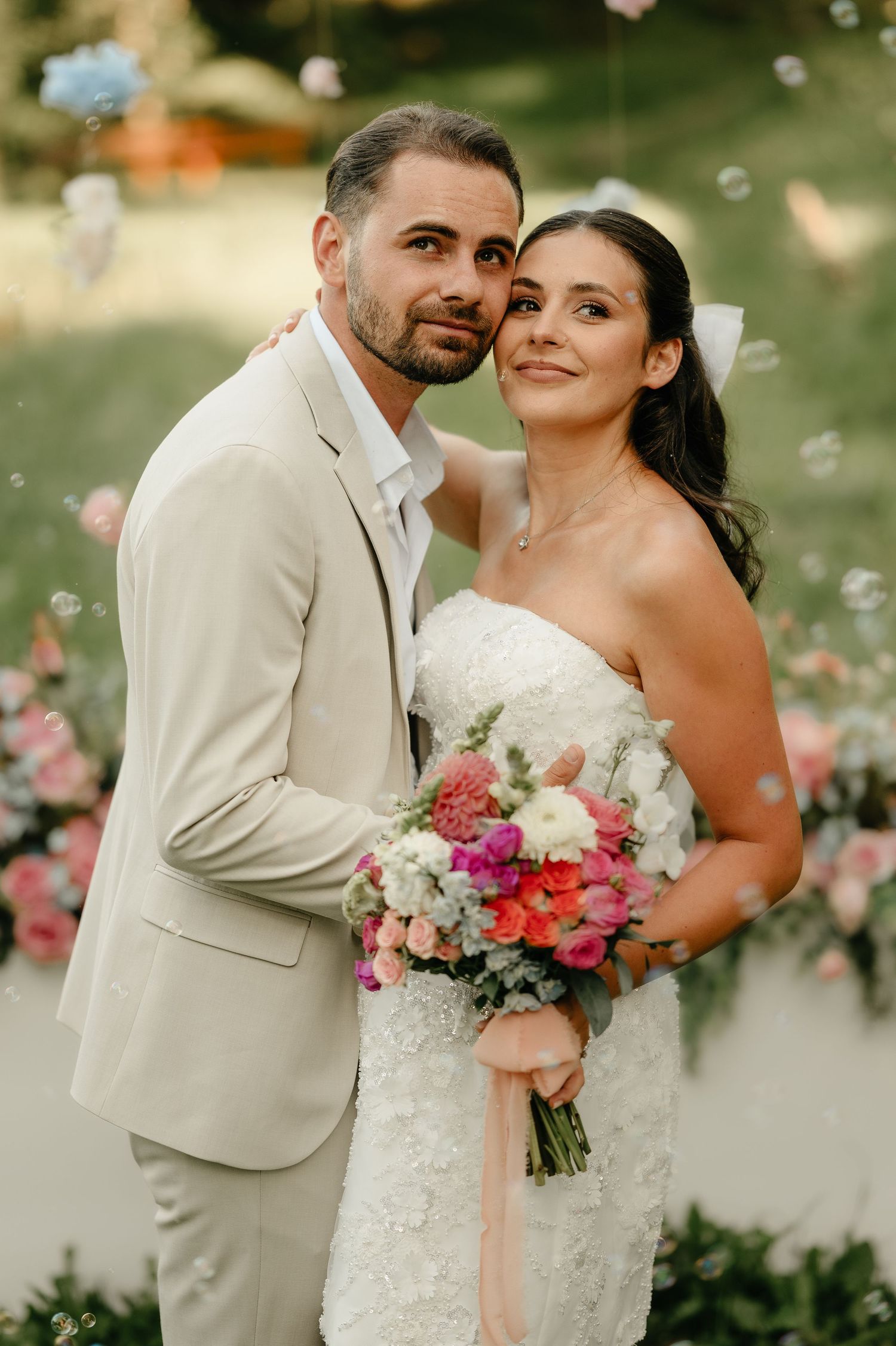 Bride and groom pose together holding a vibrant pink and white bouquet at outdoor wedding.