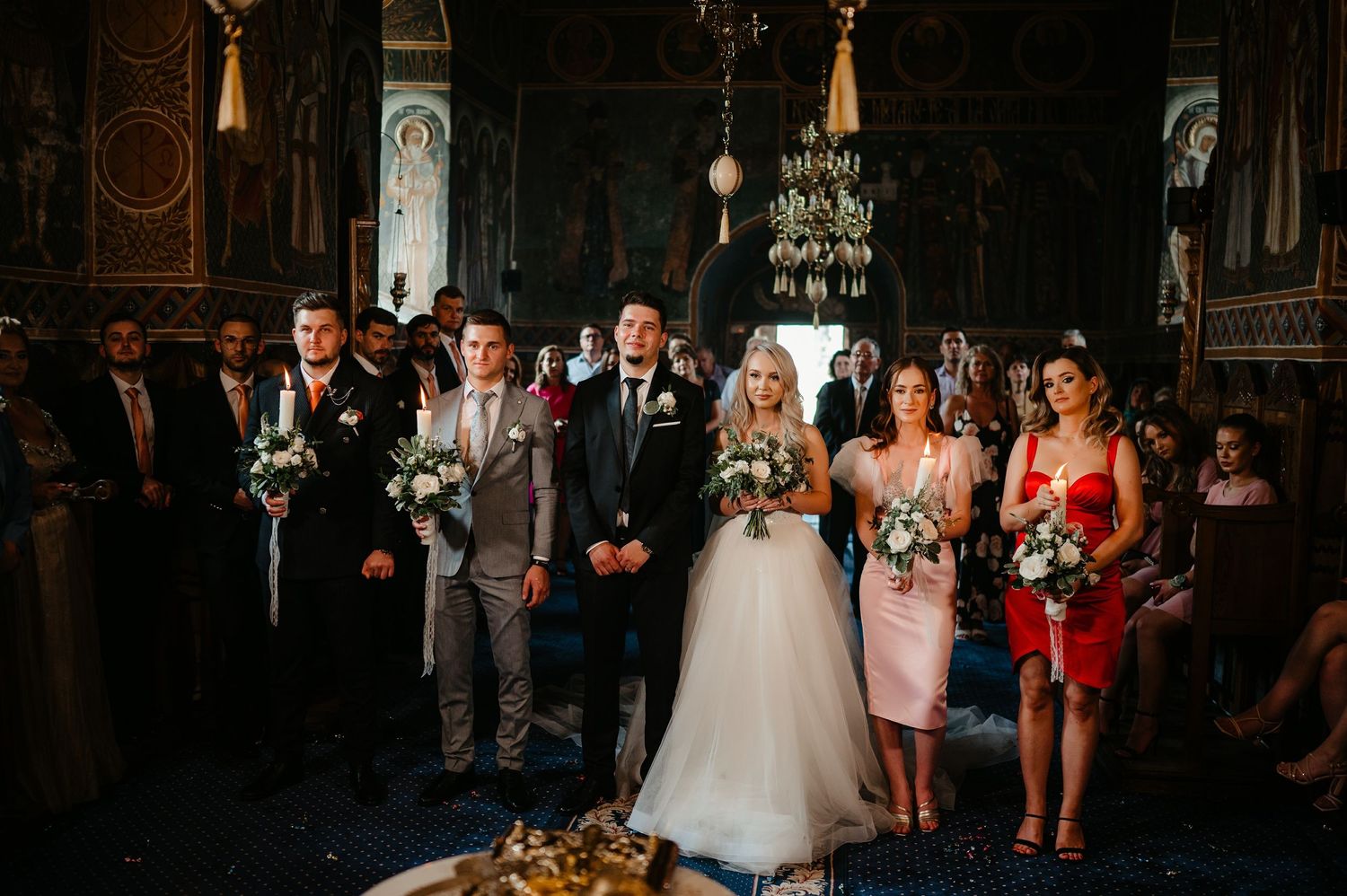 Wedding party standing at altar in ornate Orthodox church during ceremony.