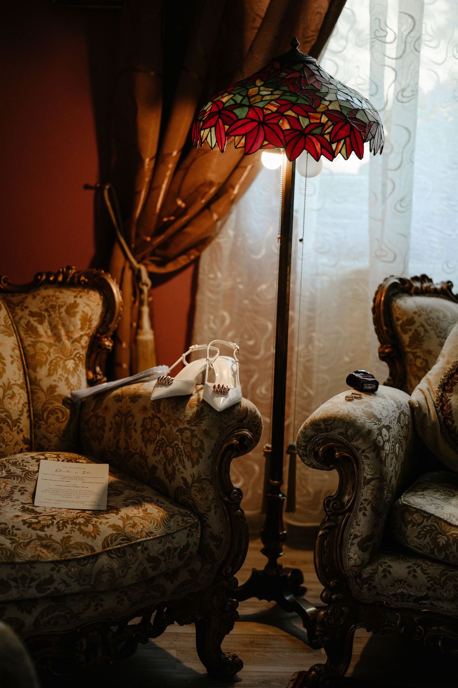 Ornate vintage armchairs with Tiffany-style stained glass floor lamp in elegant wedding preparation room.