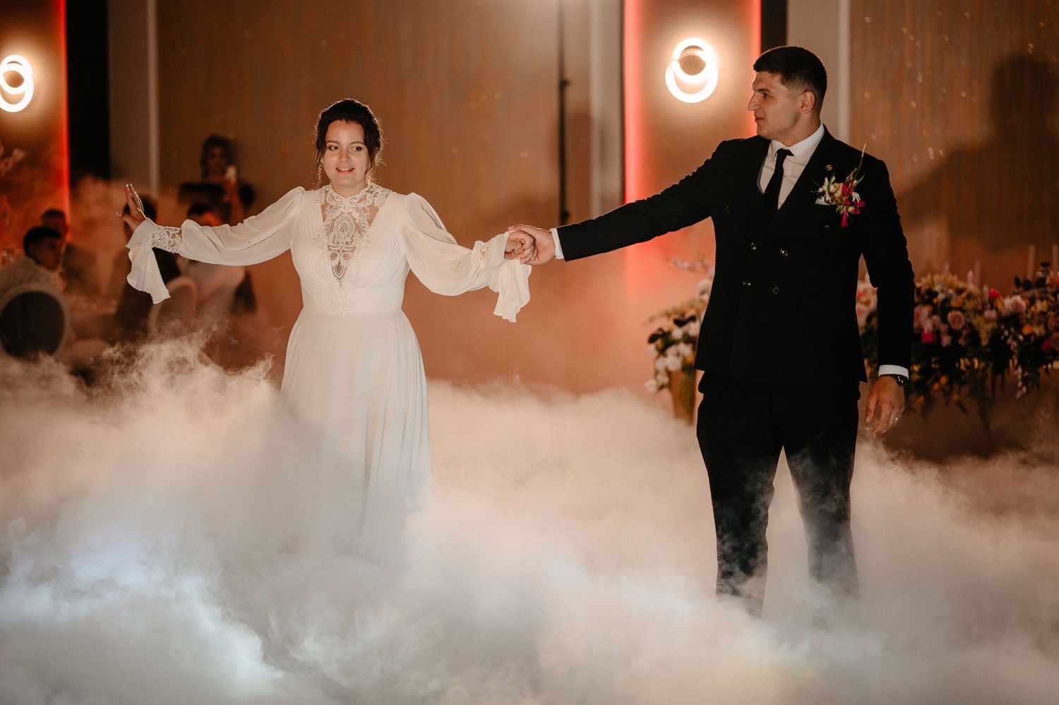 Bride and groom share first dance surrounded by dramatic fog effect on elegant wedding reception floor.