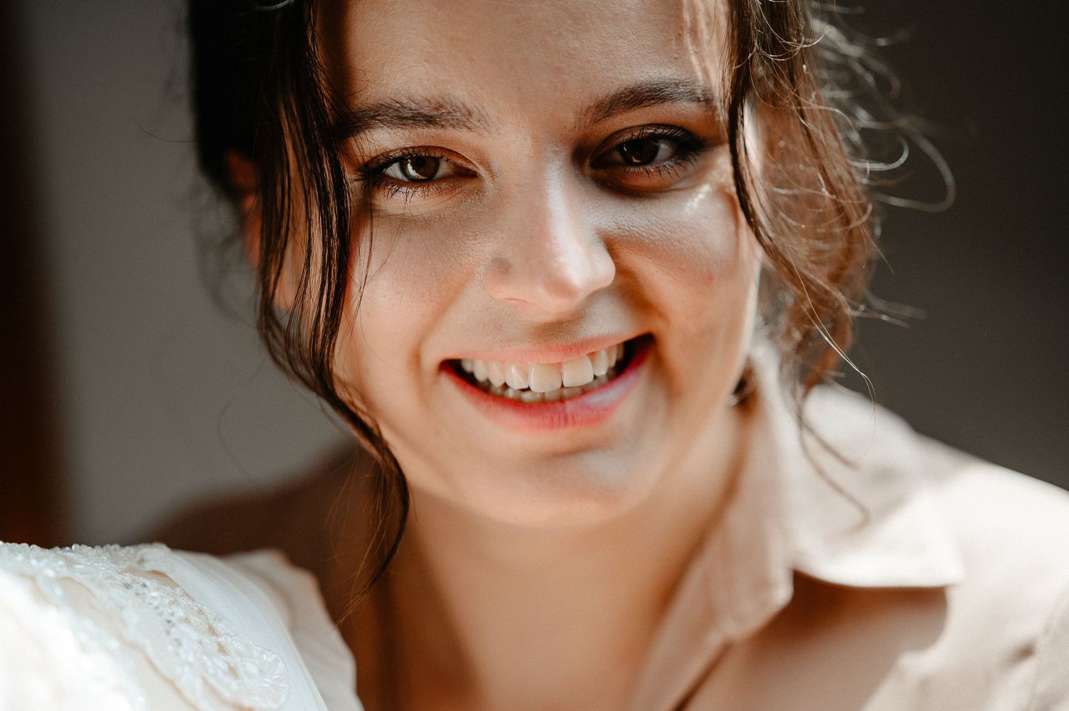 Close-up portrait of a smiling young woman with brown hair and natural makeup, wearing a light beige top.