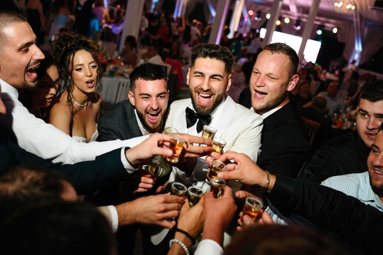 Group of wedding guests in formal attire toasting drinks together at a festive reception celebration.