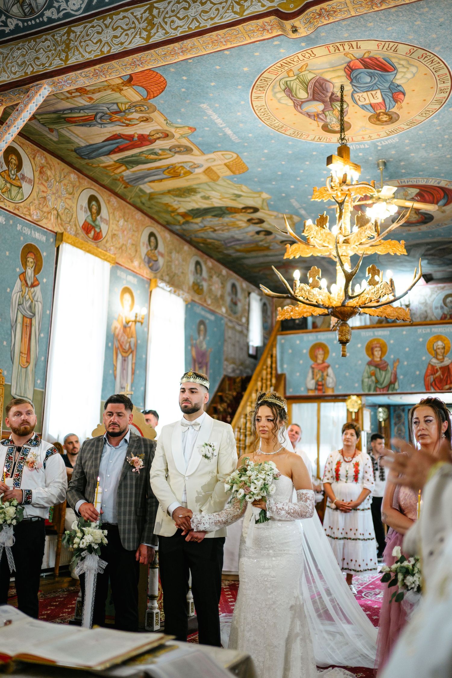 Bride and groom stand at the altar of an ornate Orthodox church with frescoed ceilings during their wedding ceremony.