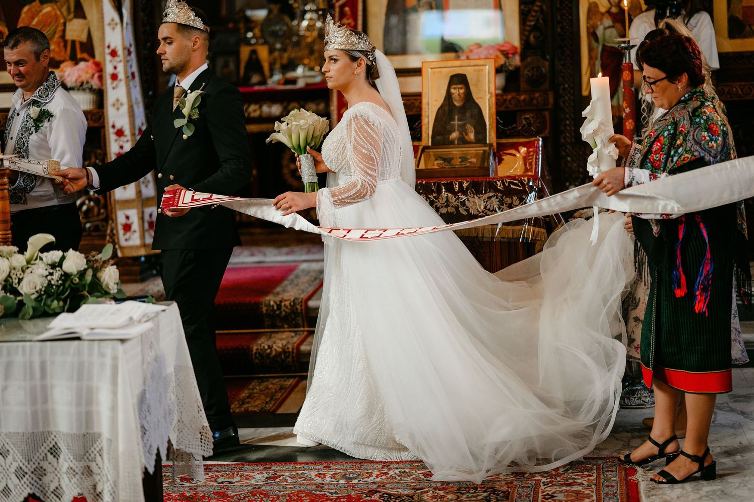 Bride and groom walking through Orthodox church ceremony with traditional red and white ribbon ritual.