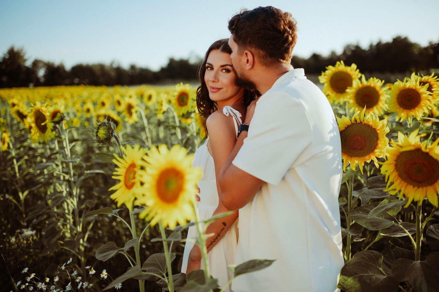 Romantic couple embracing and smiling together in a vibrant sunflower field during golden hour.