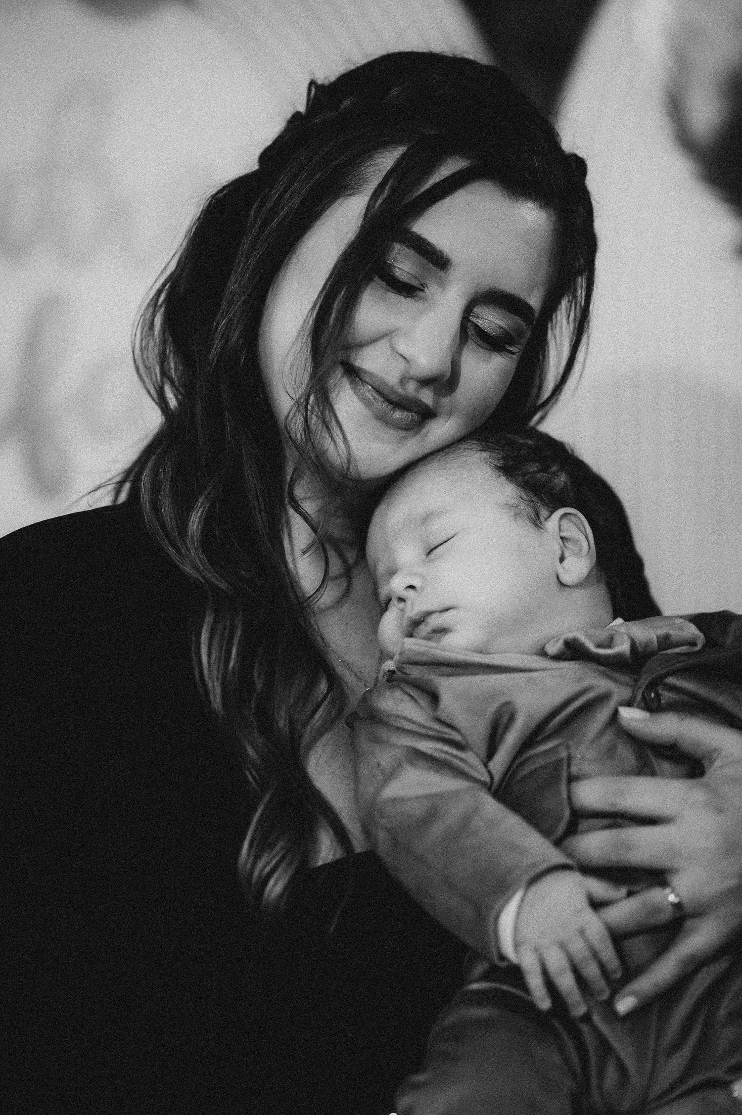 Black and white portrait of smiling mother tenderly holding sleeping newborn baby close to her face.