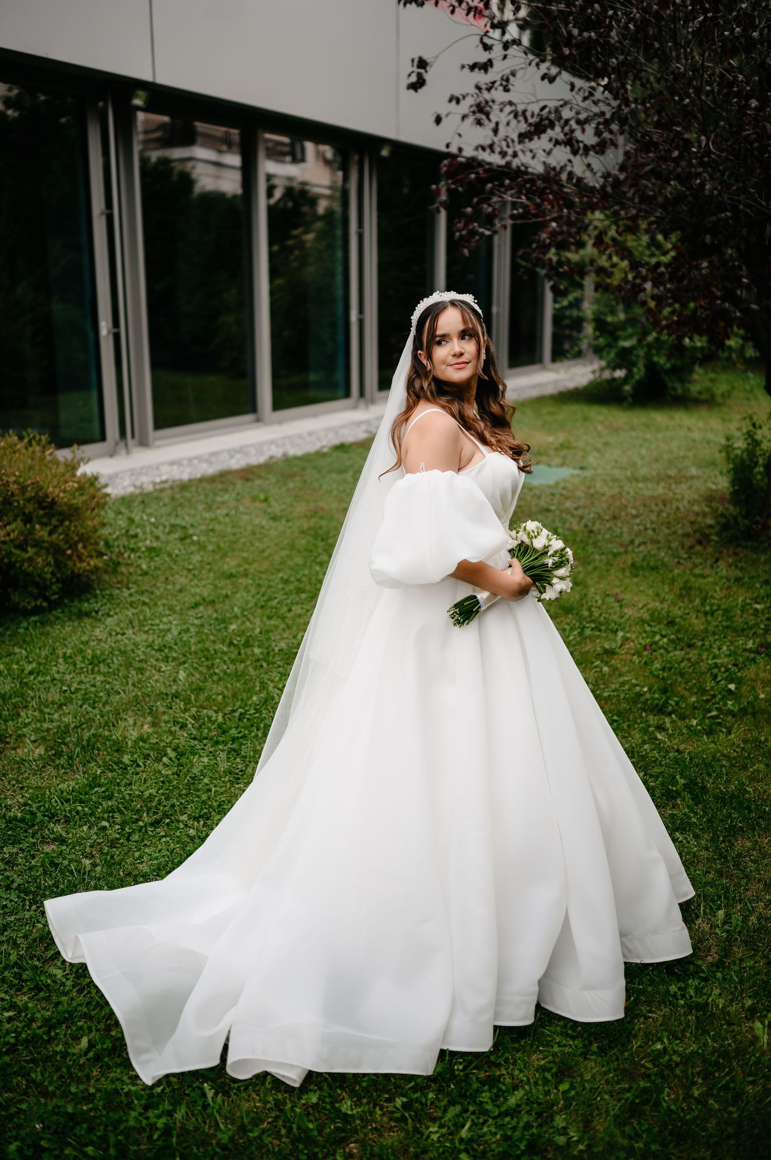 Bride in elegant white ball gown with long train and veil in garden.