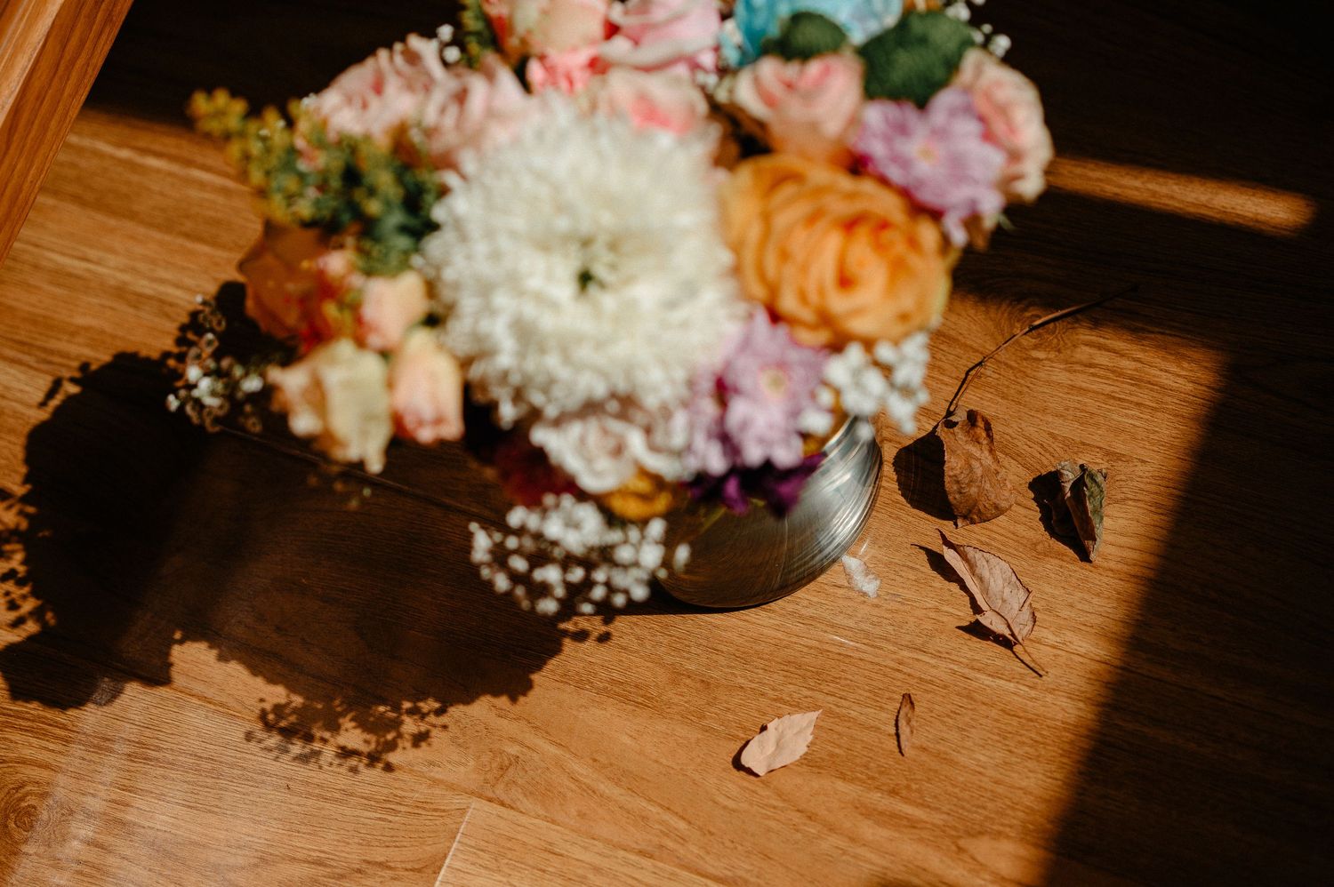 Colorful wedding bouquet with pink, white, and peach flowers on a wooden floor with scattered petals.