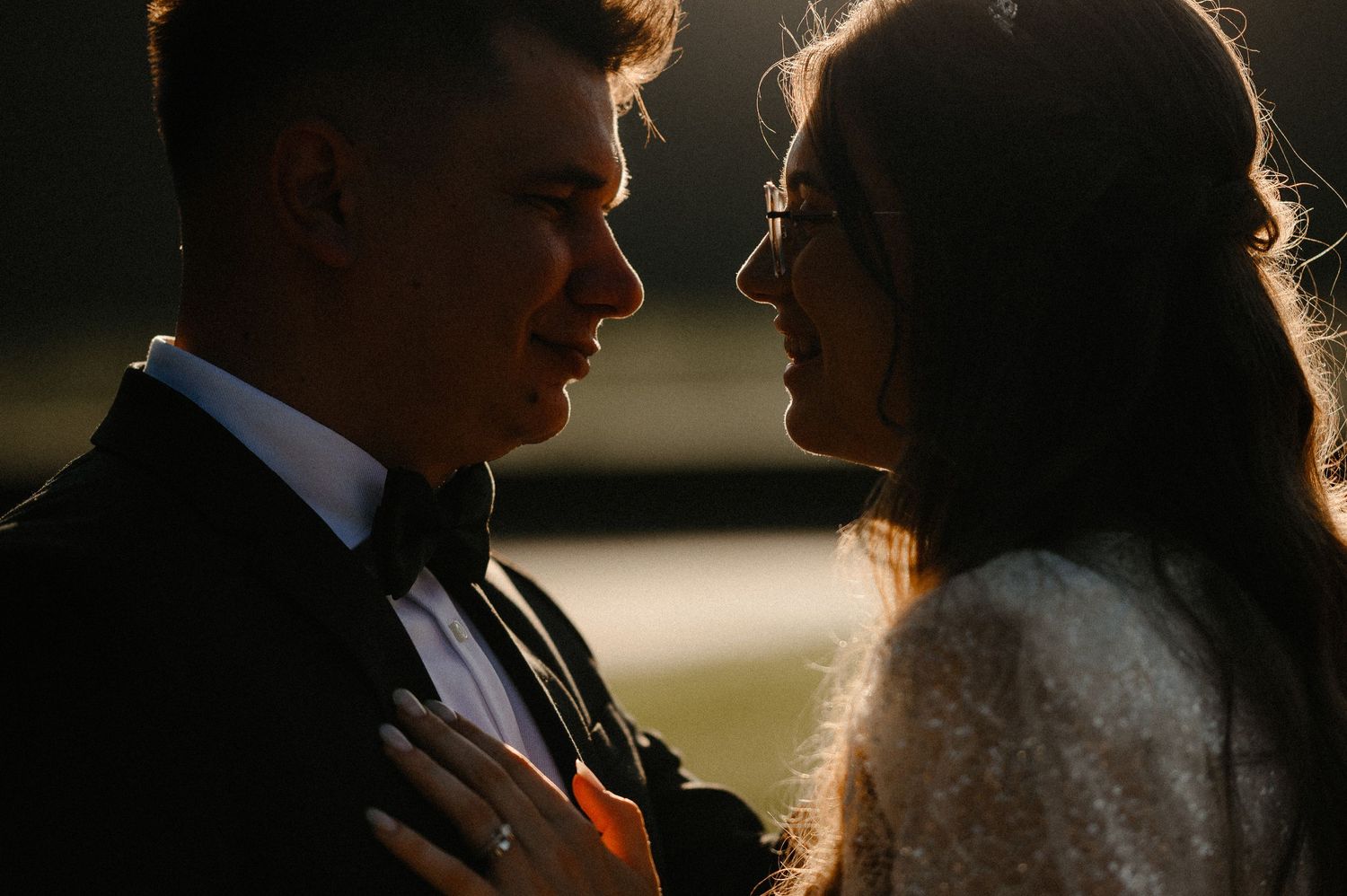 Intimate close-up of bride and groom gazing at each other in warm golden backlight.