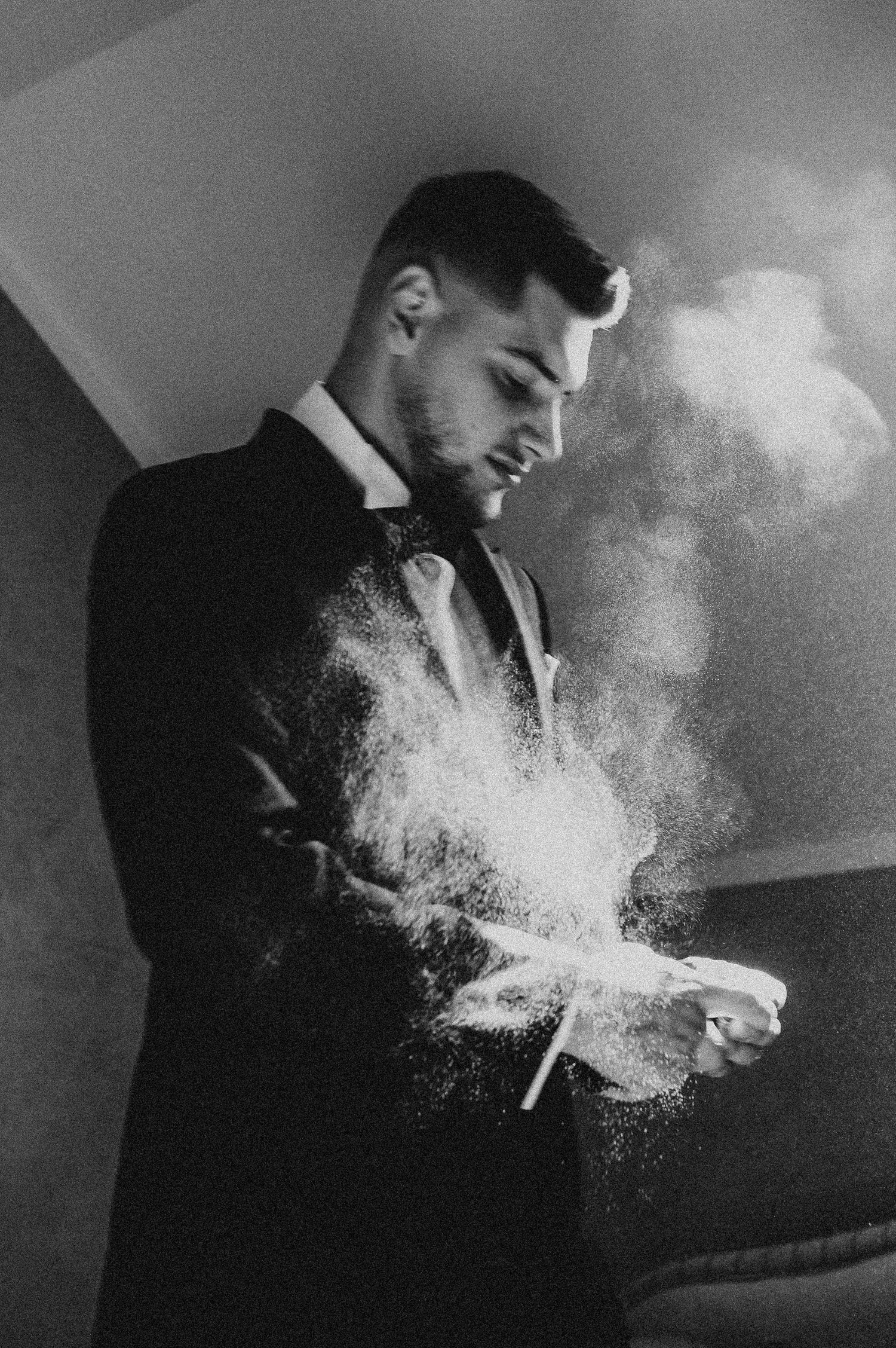 Black and white photo of groom in suit with powder explosion effect.