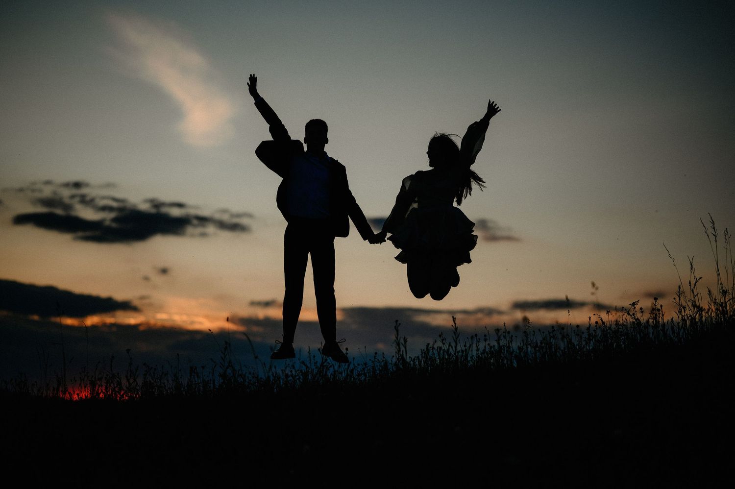 Silhouette of a couple jumping joyfully against a vibrant sunset sky.