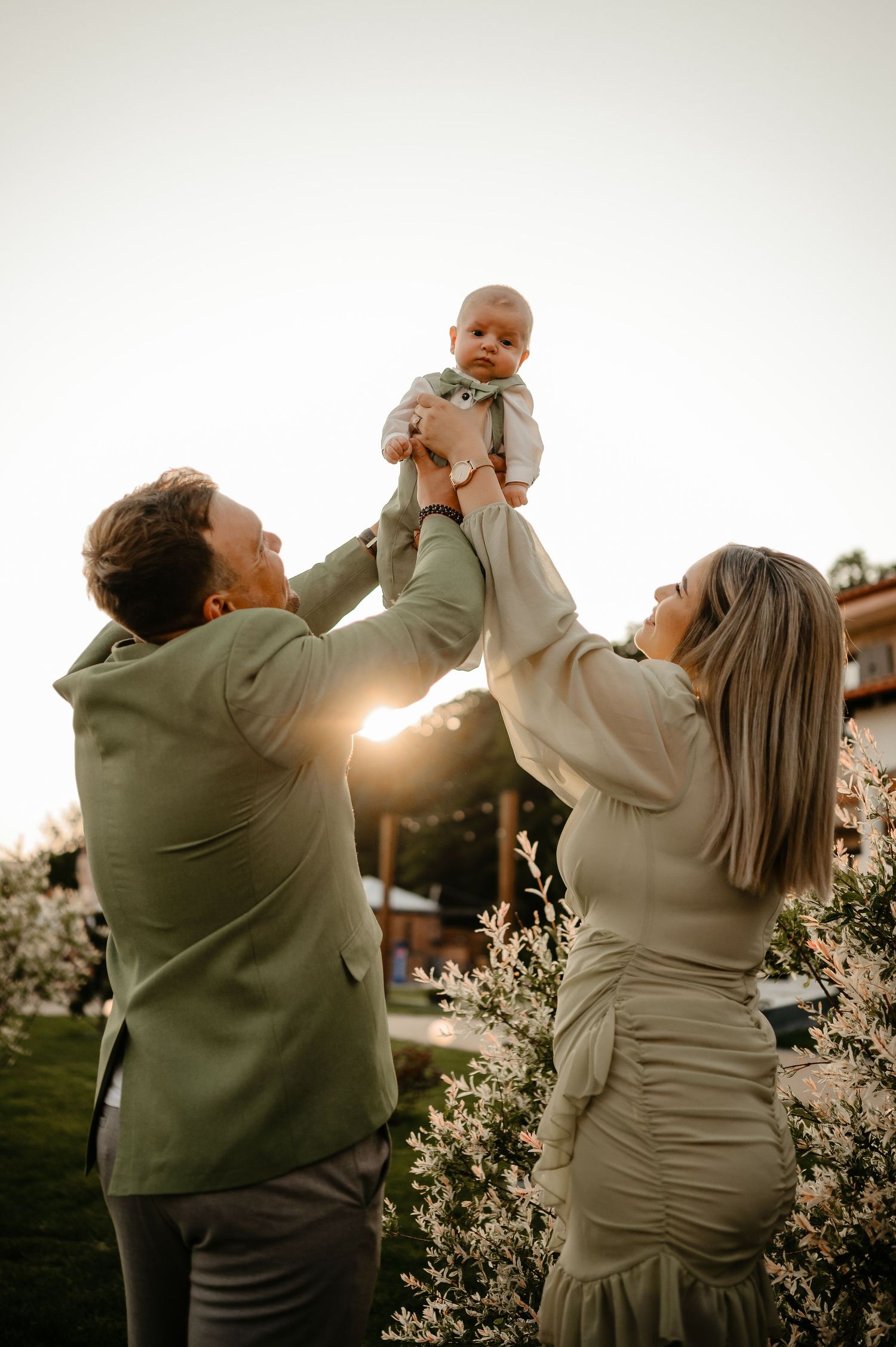 Happy parents lift their newborn baby up in the air together during a golden hour outdoor photo session.